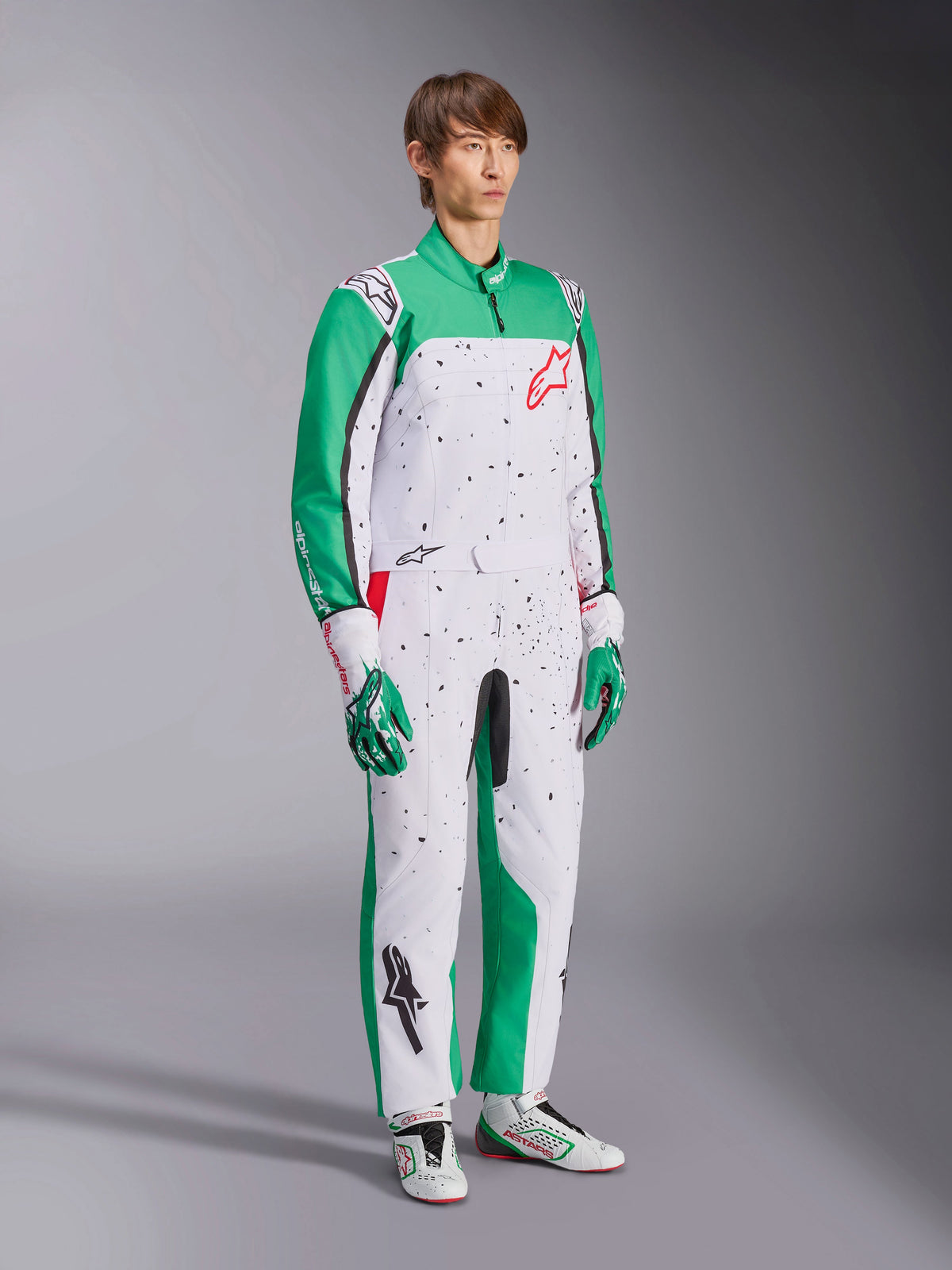 Alpinestars KMX-9 V3 Graphic 6 Anzug, Karting-Anzug, Weiß, Grün und Rot, getragen mit passenden Rennhandschuhen und Schuhen, weißes Design mit grünen Ärmeln und schwarzen Splatter-Grafiken, rotes Alpinestars-Logo auf der Brust, sportliches einteiliges Design für den Motorsport