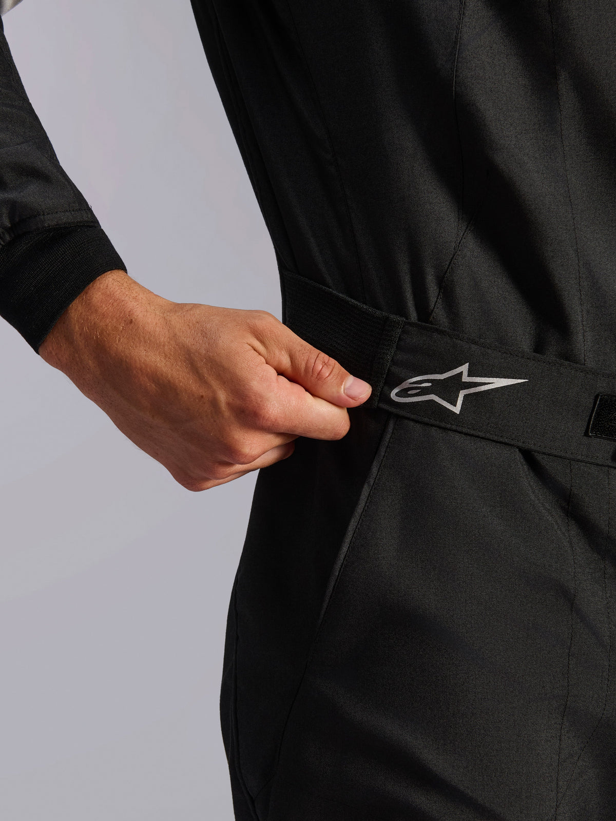 Alpinestars Limited Edition Lamborghini GP Tech V4 Anzug FIA, Automobil-Rennanzug, Schwarz, Nahaufnahme der elastischen Taillenkonstruktion, die von Hand für eine eng anliegende Passform angepasst wird, mit einem silbernen Alpinestars-Logo auf dem Gürtel