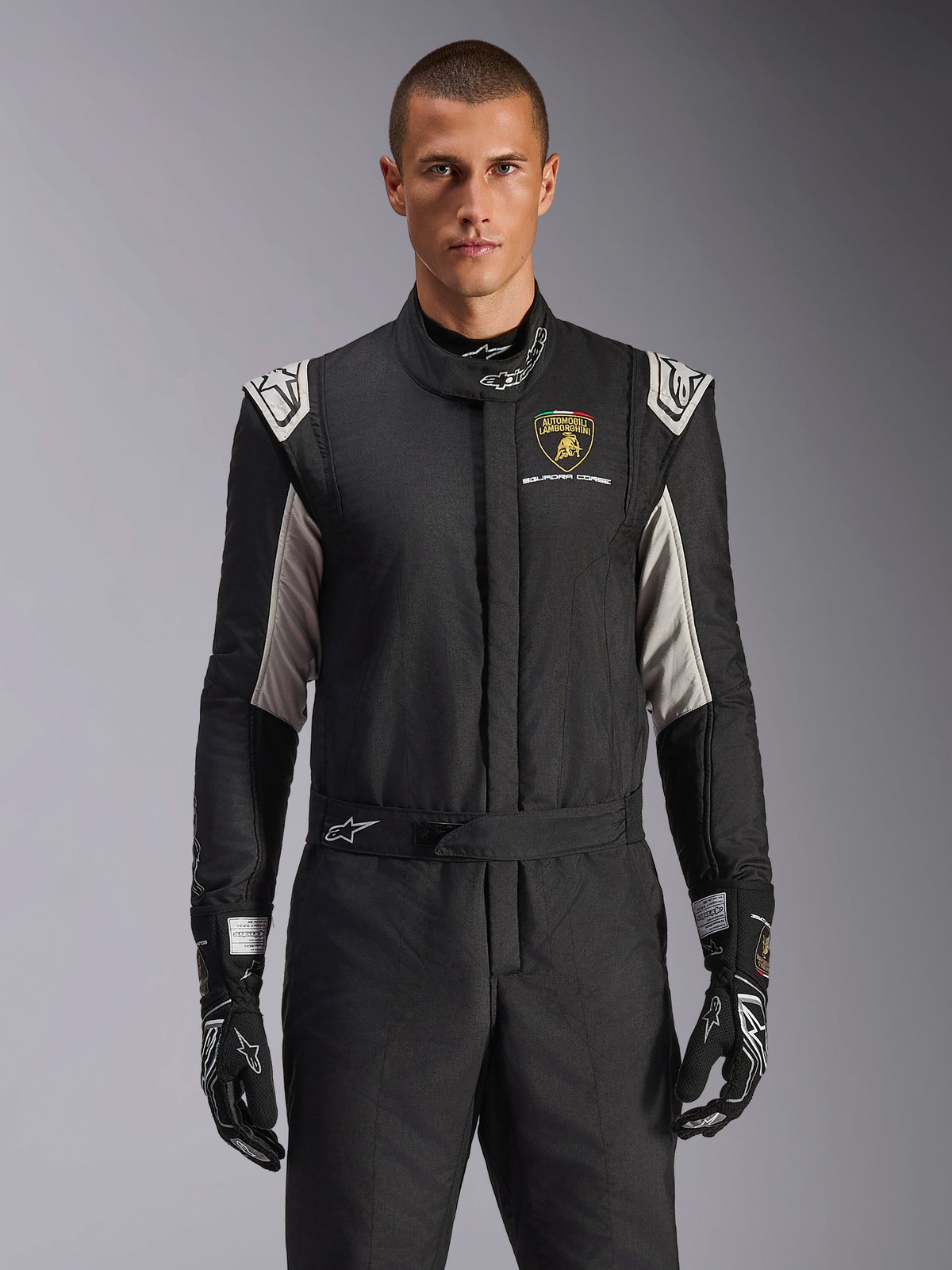 Alpinestars Limited Edition Lamborghini GP Tech V4 Anzug, professioneller Rennanzug in Schwarz mit silbernen und goldenen Akzenten, mit dem Automobili Lamborghini Squadra Corse Wappen auf der Brust, getragen von einem Model mit passenden schwarzen Rennhandschuhen