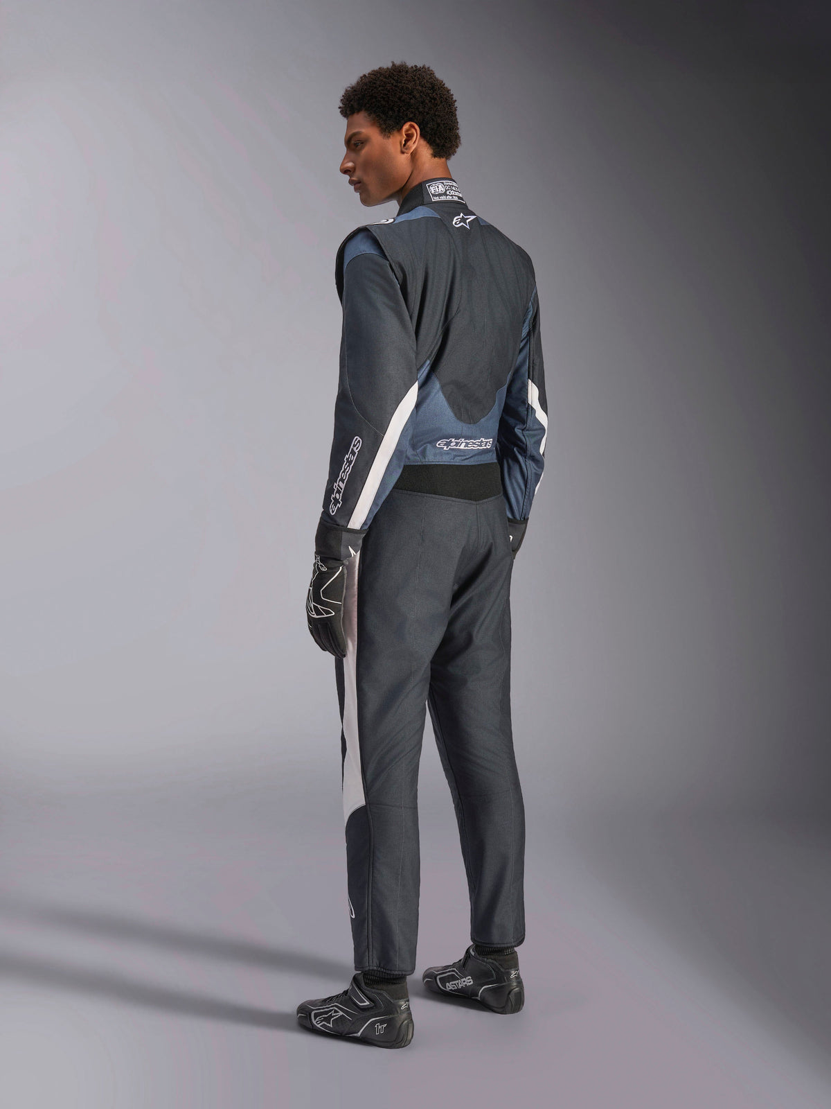 Alpinestars GP Pro Comp V2 FIA Autorennsport-Anzug, Schwarz und Asphalt mit weißen Akzenten, 3/4-Rückansicht eines Models.