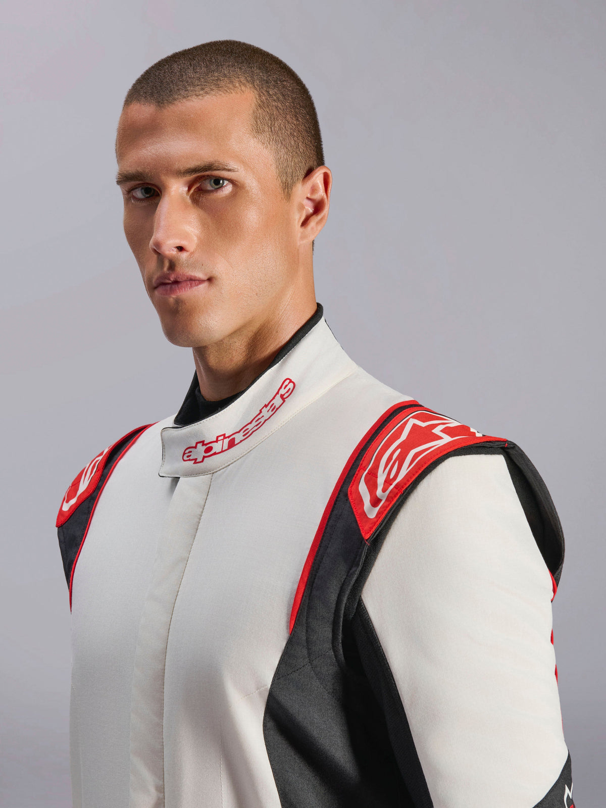 Alpinestars GP Tech V4 Anzug, Auto-Rennanzug, Weiß, Schwarz und Rot, von einem Model getragen, mit roten Schulterpartien mit Alpinestars-Logo, weißem Torso mit schwarzen Seiteneinsätzen und Kragen mit Markenschriftzug, professionelle Motorsportausrüstung