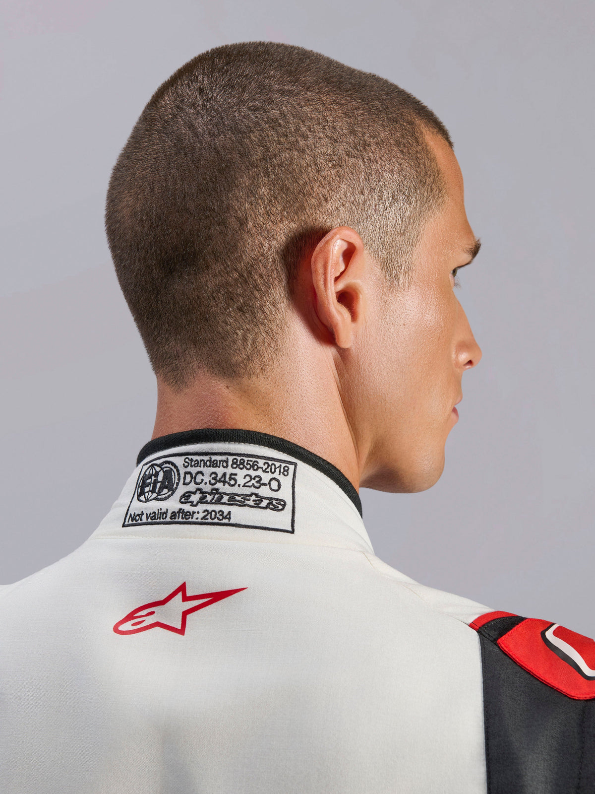 Alpinestars GP Tech V4 Anzug, Weiß-Schwarz-Roter Auto-Rennanzug, Nahaufnahme des hinteren Kragens mit FIA 8856-2018 Zertifizierungsetikett und rotem Stern-Logo, professionelle Motorsport-Schutzausrüstung