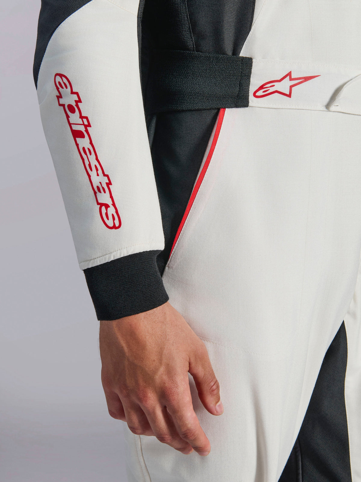 Alpinestars GP Tech V4 Suit, Weiß-Schwarz-Roter Auto-Rennanzug, Nahaufnahme von Ärmel und Taille, mit rotem Alpinestars-Schriftzug und Stern-Logo, elastischer Bund mit Klettverschluss und roten Akzentpaspeln auf weißem und schwarzem technischem Gewebe