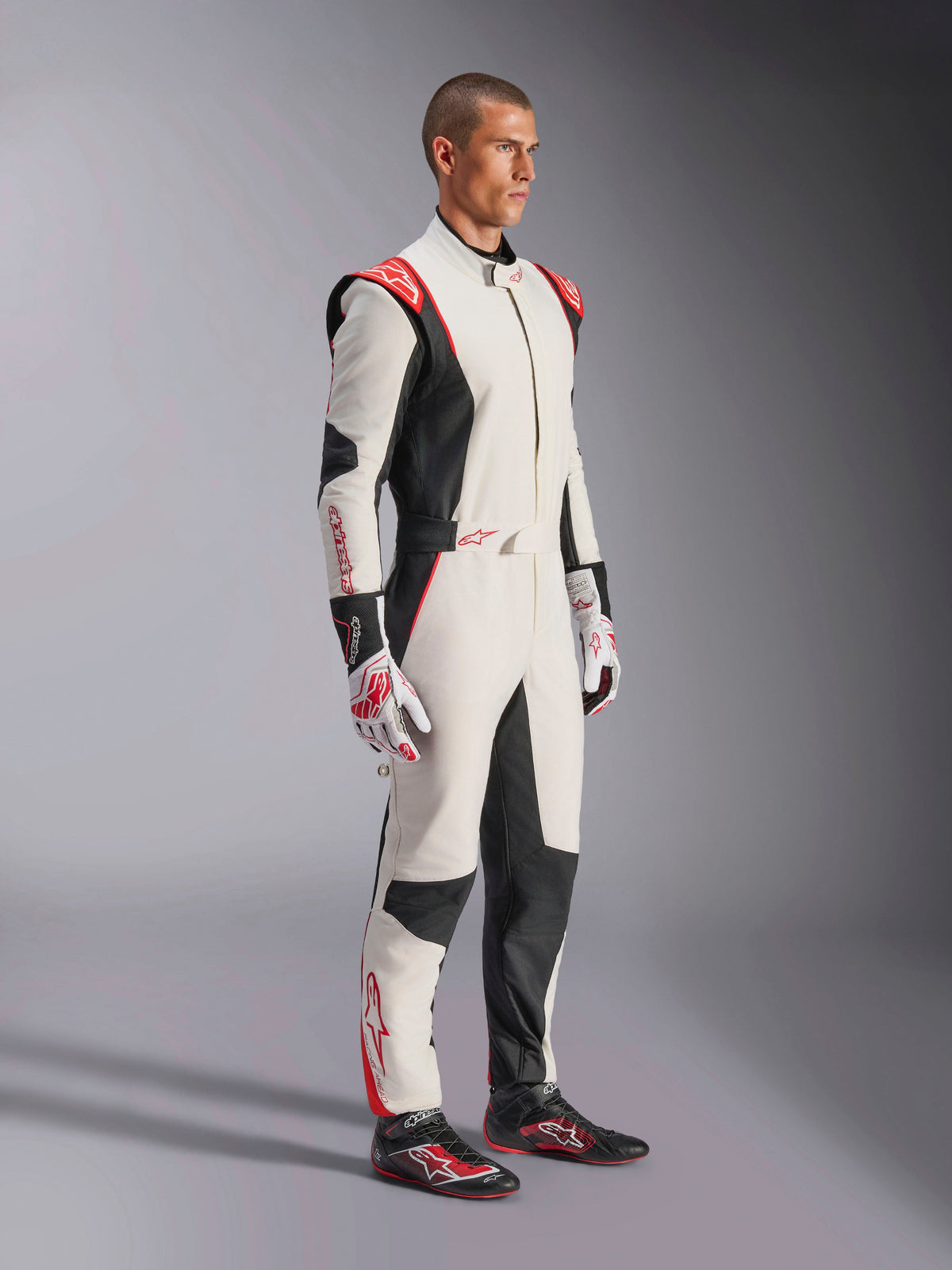 Männlicher Rennfahrer im Alpinestars GP Tech V4 Anzug, Weiß, Schwarz und Rot, einteiliger Auto-Rennanzug, passende Handschuhe und Rennschuhe, professionelle Motorsportausrüstung mit Alpinestars-Branding und ergonomischem Design