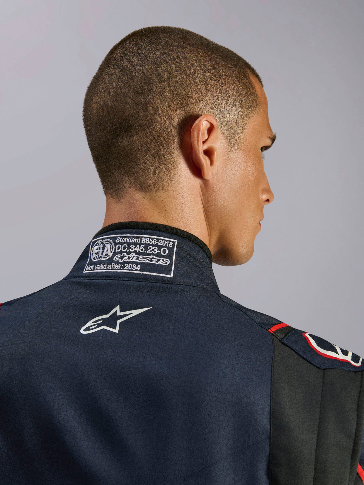 Alpinestars GP Tech V4 Anzug in Blau Navy Schwarz Rot, Nahaufnahme des hinteren Kragens mit dem FIA 8856-2018 Zertifizierungslabel und weiß gesticktem Alpinestars-Logo, Detail eines Hochleistungs-Autorennanzugs