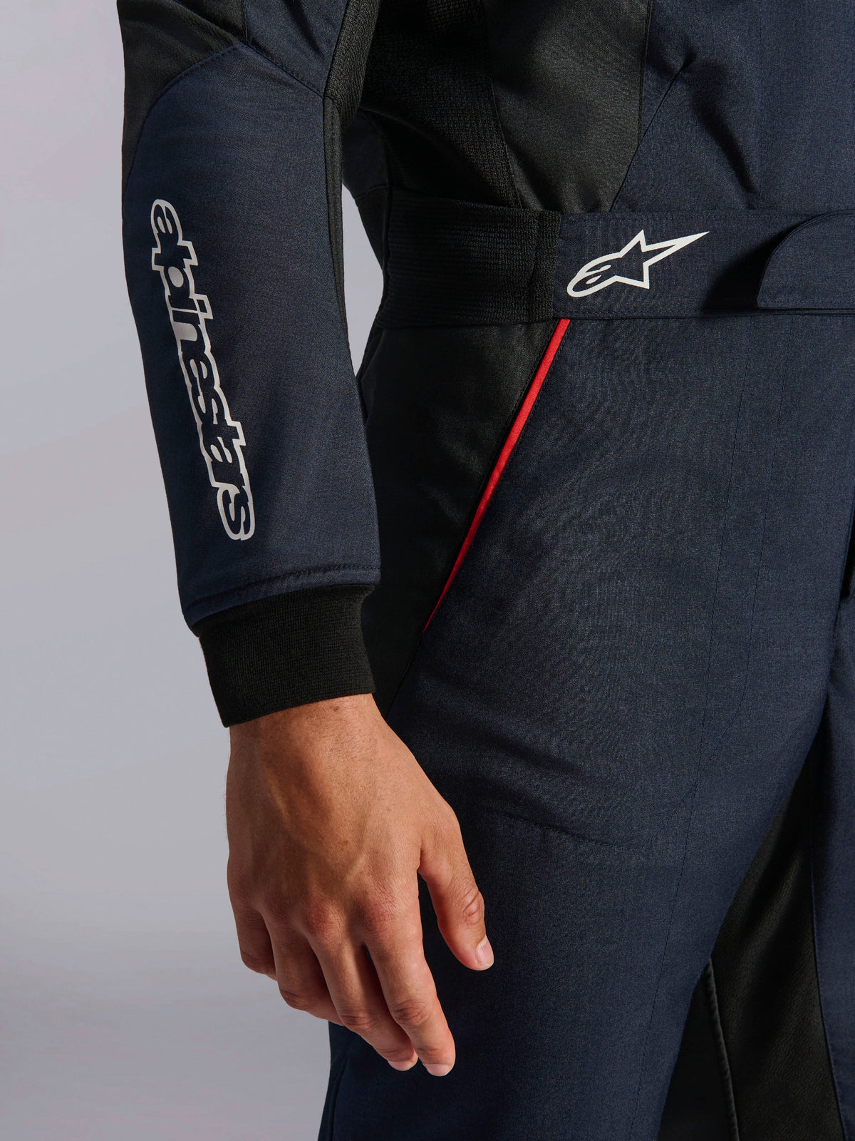 Alpinestars GP Tech V4 Anzug in Blue Navy Black Red, Detailaufnahme von Taille und Ärmel mit weißen Alpinestars-Logos, roten Akzentpaspeln und strukturiertem Twill-Gewebe.