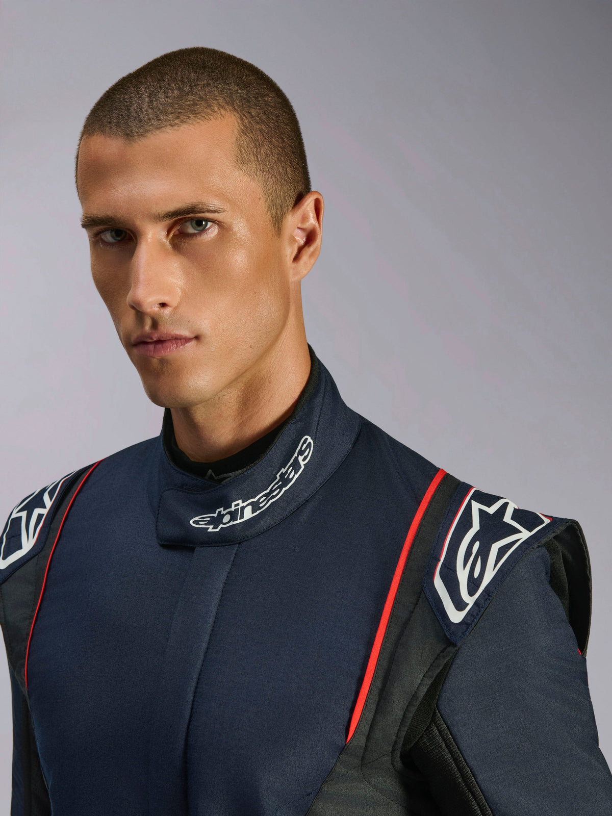 Nahaufnahme-Porträt eines Models im Alpinestars GP Tech V4 Anzug, Auto-Rennanzug in Navy-Blau, Schwarz und Rot, mit Alpinestars-Branding am hohen Kragen und strukturierten Schulterklappen.