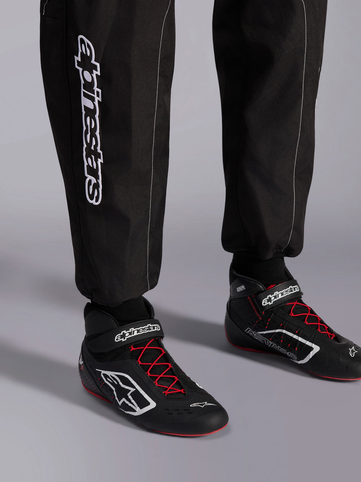 Alpinestars KMX-9 V3 Suit, Karting Suit, Black Red and White, detail view of lower legs and karting boots, white Alpinestars branding on the side, black shoes with red laces and white accents, professional motorsport racing gear.