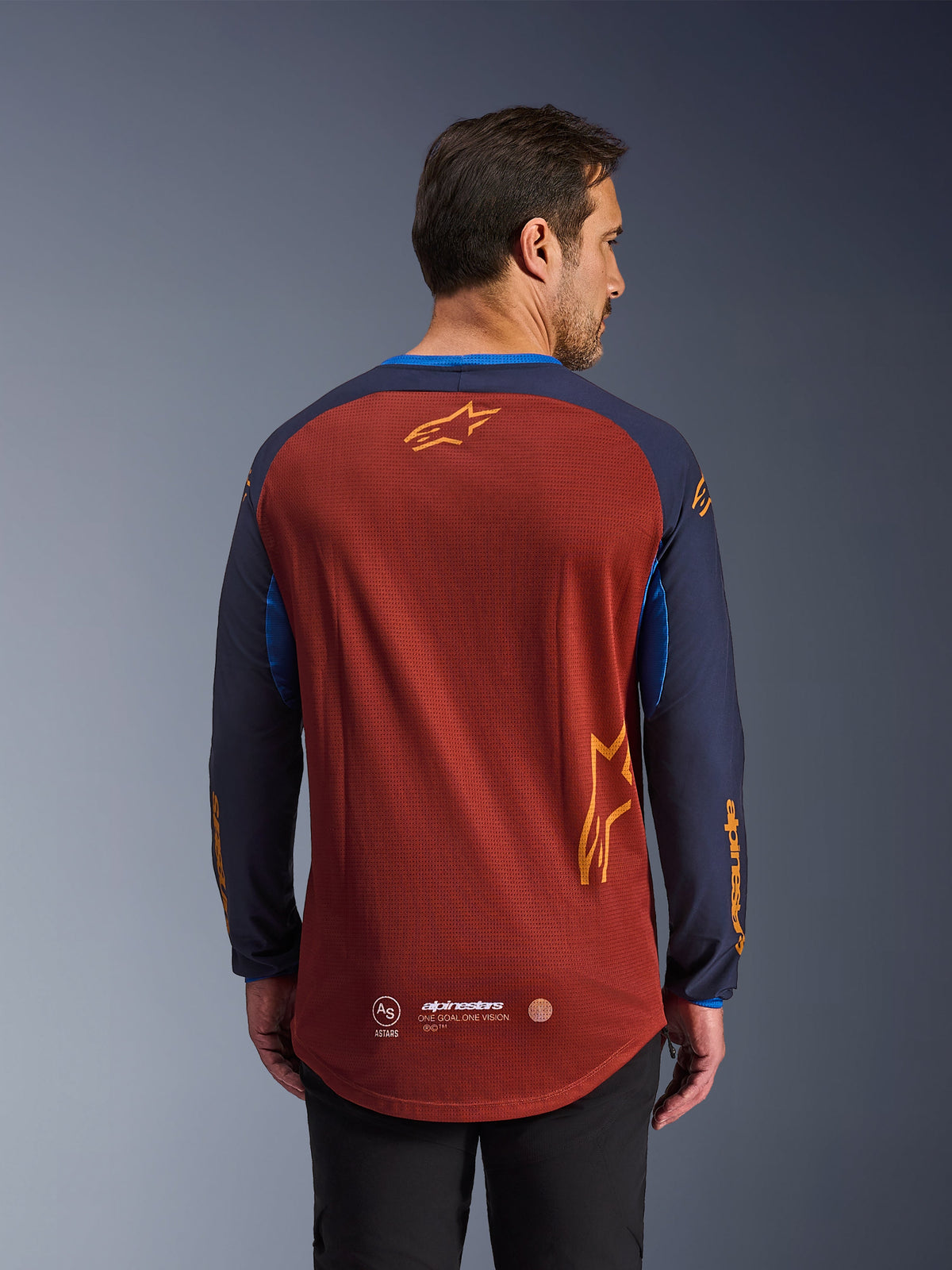 Alpinestars Maxdura Dual Trikot in Rostbraun und Mood Indigo, Rückansicht, mit einem atmungsaktiven Mesh-Torso, dunkelblauen Ärmeln mit orangefarbenem Alpinestars-Branding und einem abgesenkten Saum im Rückenbereich für zusätzliche Abdeckung.