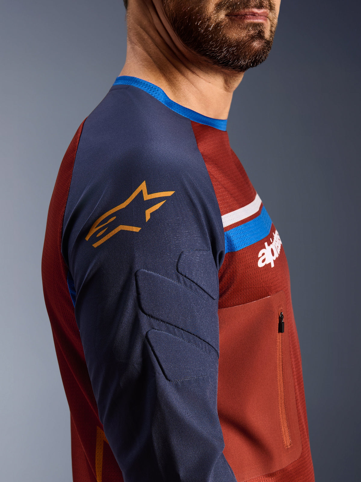 Alpinestars Maxdura Dual Jersey, Rostbraun und Mood Indigo, Seitenansicht mit gepolsterten Ärmeln und gelbem Stern-Logo, Mesh-Torso-Konstruktion mit Reißverschluss-Brusttasche, technische Motorradbekleidung für Adventure-Fahrten