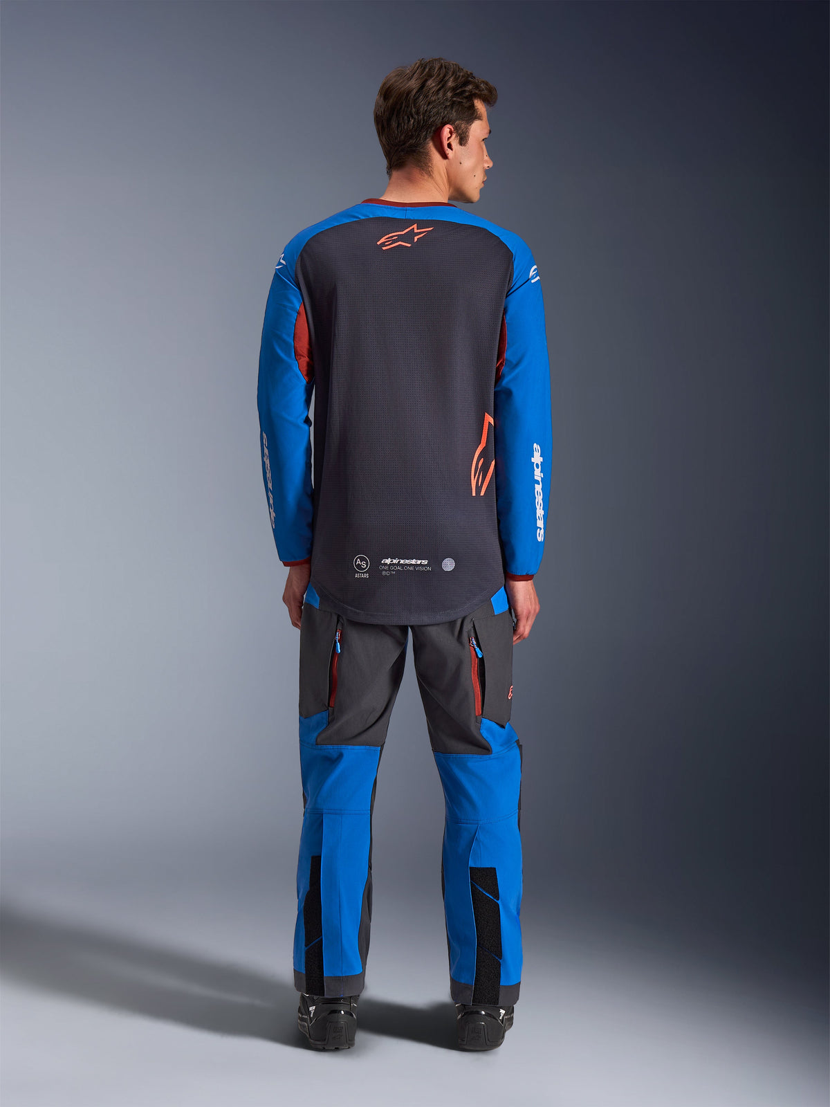 Alpinestars Maxdura Dual Jersey in Dunkelgrau und Royalblau, Rückansicht mit Full-Mesh-Torso und orangem Stern-Logo, royalblaue Ärmel mit weißem Branding, kombiniert mit passender grau-blauer Adventure-Hose, Hochleistungsausrüstung für Dual-Sport-Fahrten