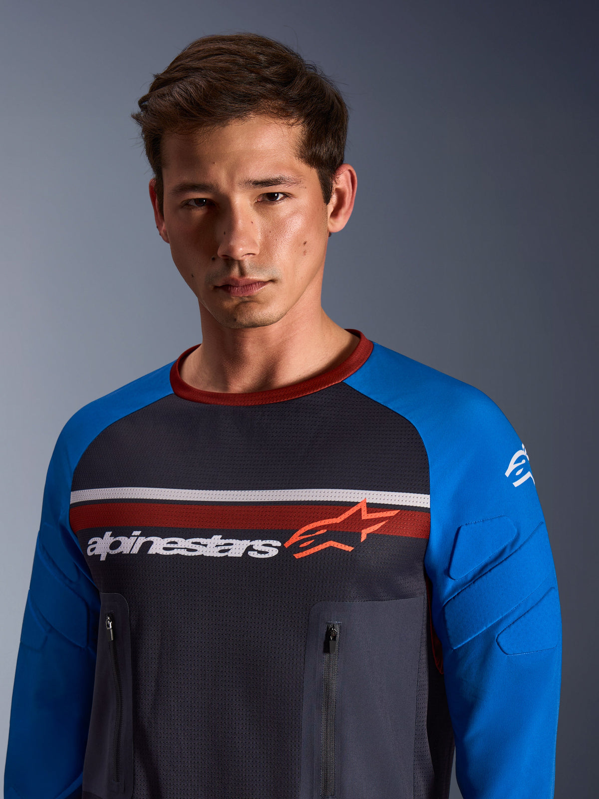 Alpinestars Maxdura Dual Jersey, Dunkelgrau und Königsblau, getragen von einem männlichen Model, Mesh-Torso, königsblaue Ärmel mit integrierter Polsterung, vertikale Brusttaschen mit Reißverschluss, Alpinestars-Branding auf der Brust