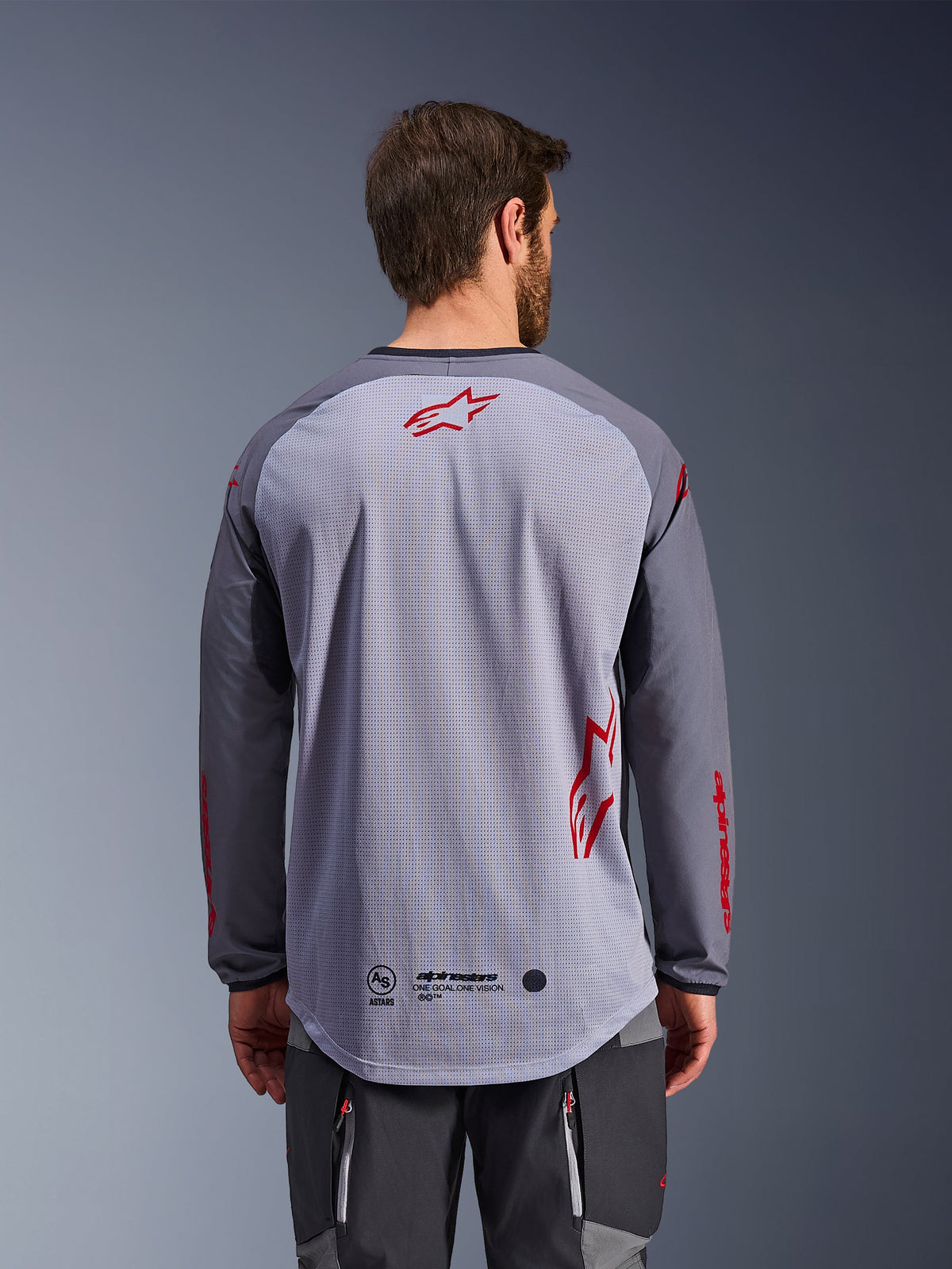Alpinestars Maxdura Dual Trikot, Rückansicht, Mittelgrau und Dunkelgrau, mit atmungsaktivem Mesh-Rücken, roten Alpinestars Stern-Logos, langen Ärmeln und verlängertem Rückensaum, Adventure-Motorradausrüstung