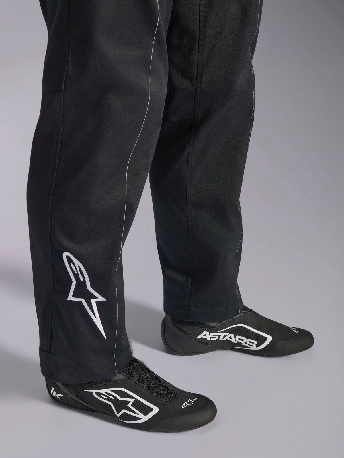 Alpinestars Kart Indoor V2 Suit, Black karting suit, close-up of lower legs and feet featuring a white Alpinestars logo on the calf, worn with matching black and white racing shoes, designed for recreational karting.