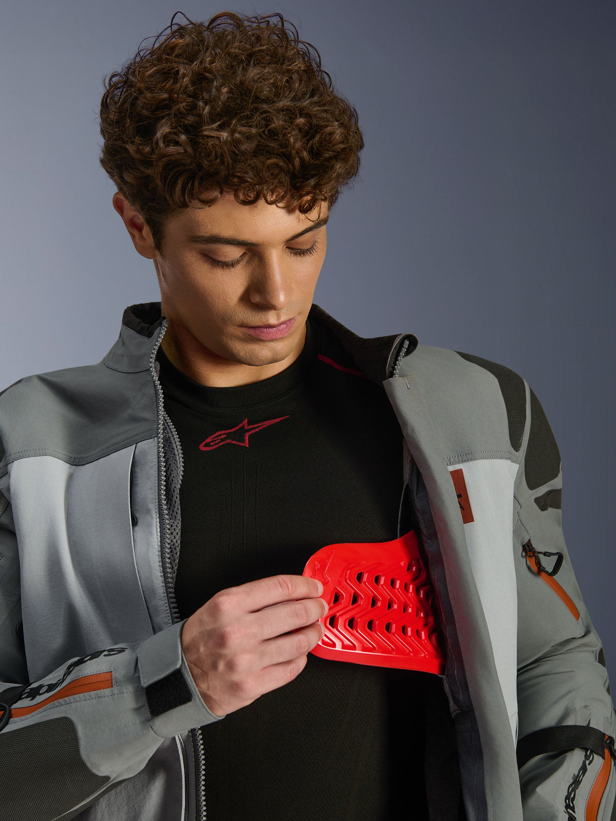 Alpinestars Nazca 3L GORE-TEX PRO Jacke, Dunkelgrau und Mittelgrau, männliches Model zeigt roten Nucleon PLASMA Pro Protektoreinsatz, Adventure-Fahrbekleidung, Premium-Motorradjacke mit technischen Details