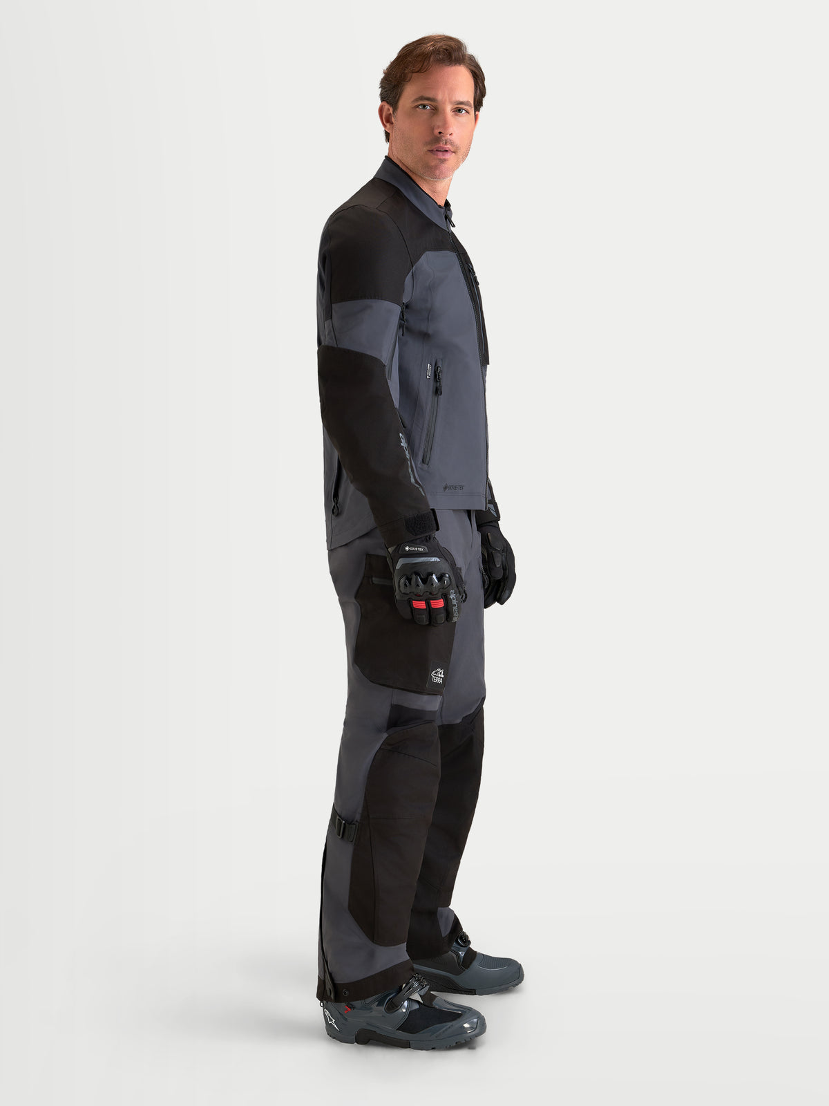 Alpinestars Arenis Gore-Tex Gear Set, Herren-Adventure-Motorradjacke und -hose in Schwarz und Dunkelgrau, Seitenprofilansicht an einem Model mit passender Ausrüstung, wasserdichte GORE-TEX Textilkonstruktion