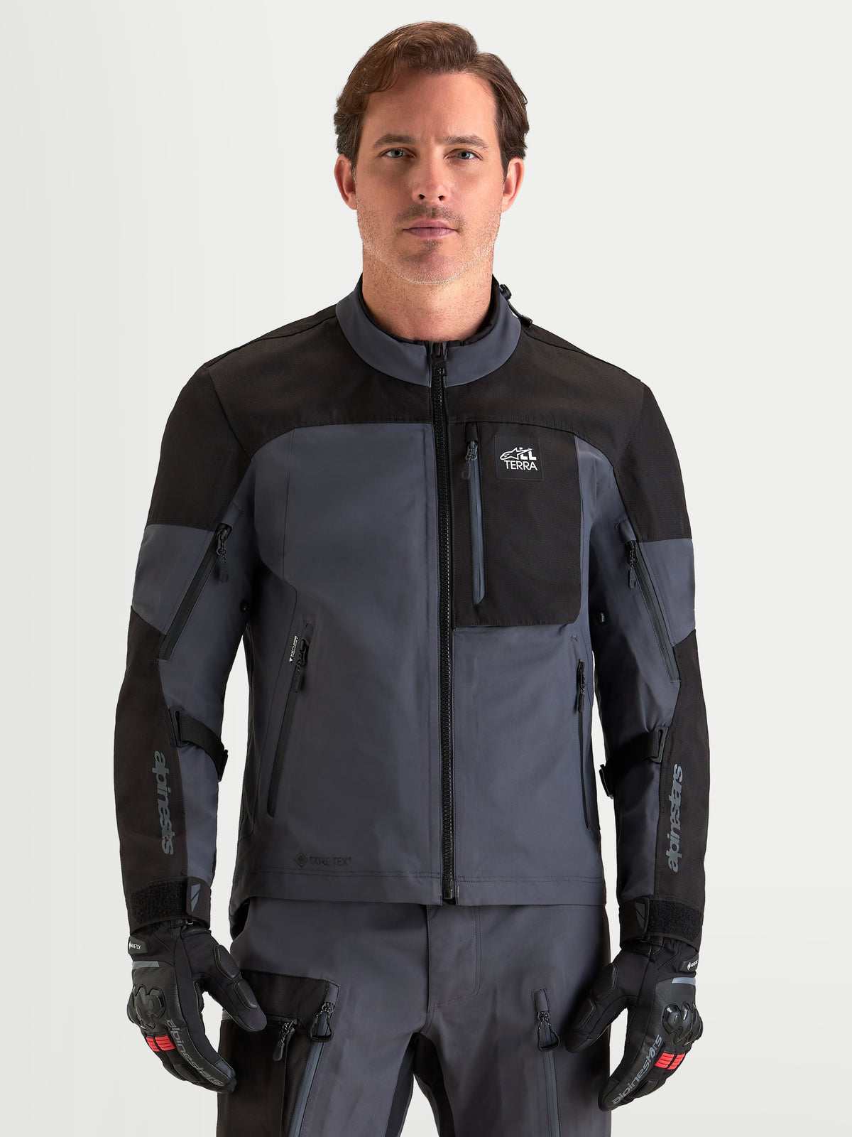 Alpinestars Arenis Gore Tex Jacke, Herren-Adventure-Motorradjacke in Schwarz und Dunkelgrau, Vorderansicht an einem Model mit passender Ausrüstung und Handschuhen, CE-zertifizierte, wasserdichte All-Terrain-Schutzausrüstung