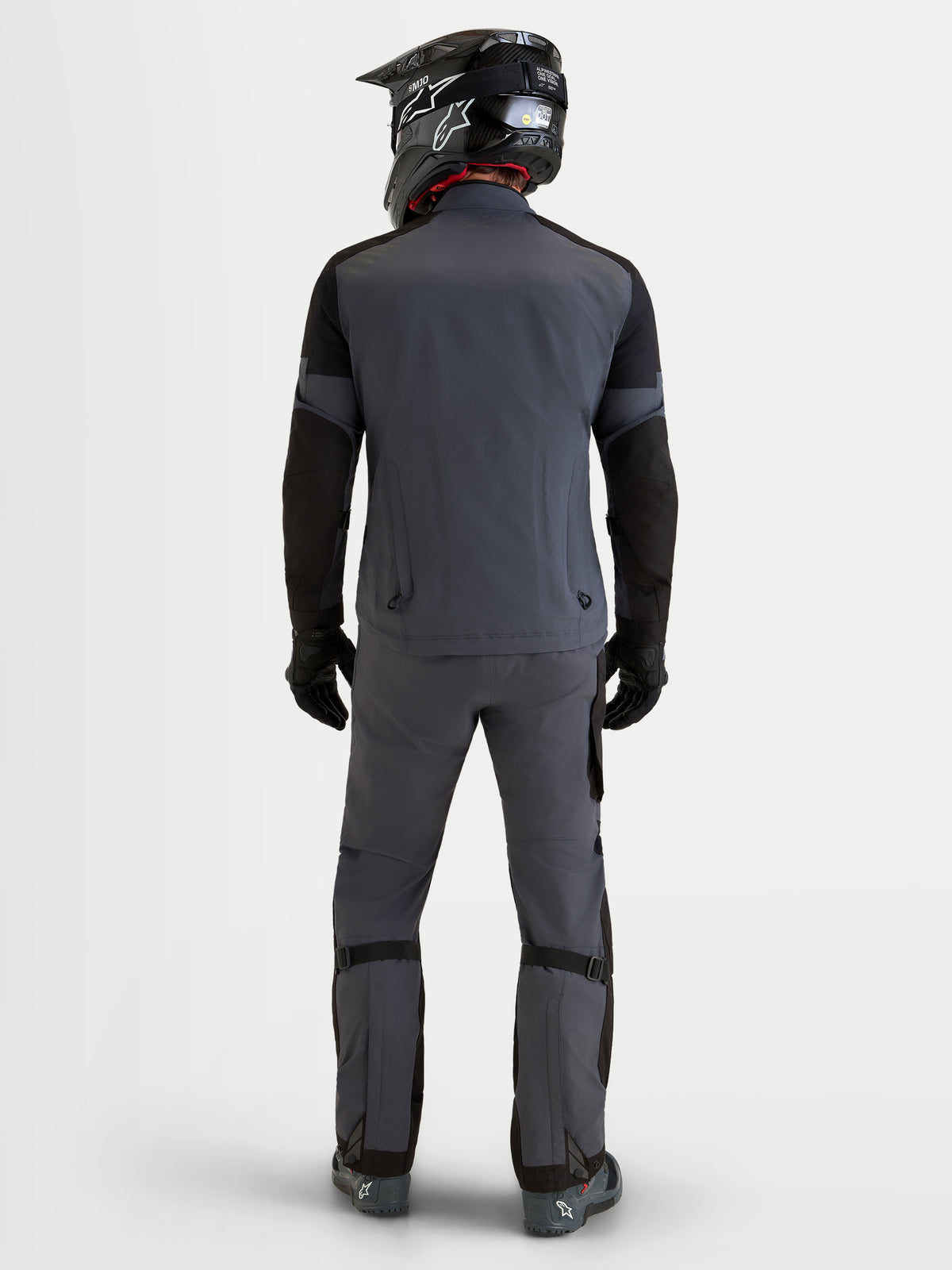 Alpinestars Arenis Gore-Tex Gear Set, Herren-Adventure-Motorradjacke und -hose in Dunkelgrau und Schwarz, Rückansicht am Model mit passendem Helm und Fahrerausrüstung, wasserdichte GORE-TEX All-Terrain-Schutzausrüstung
