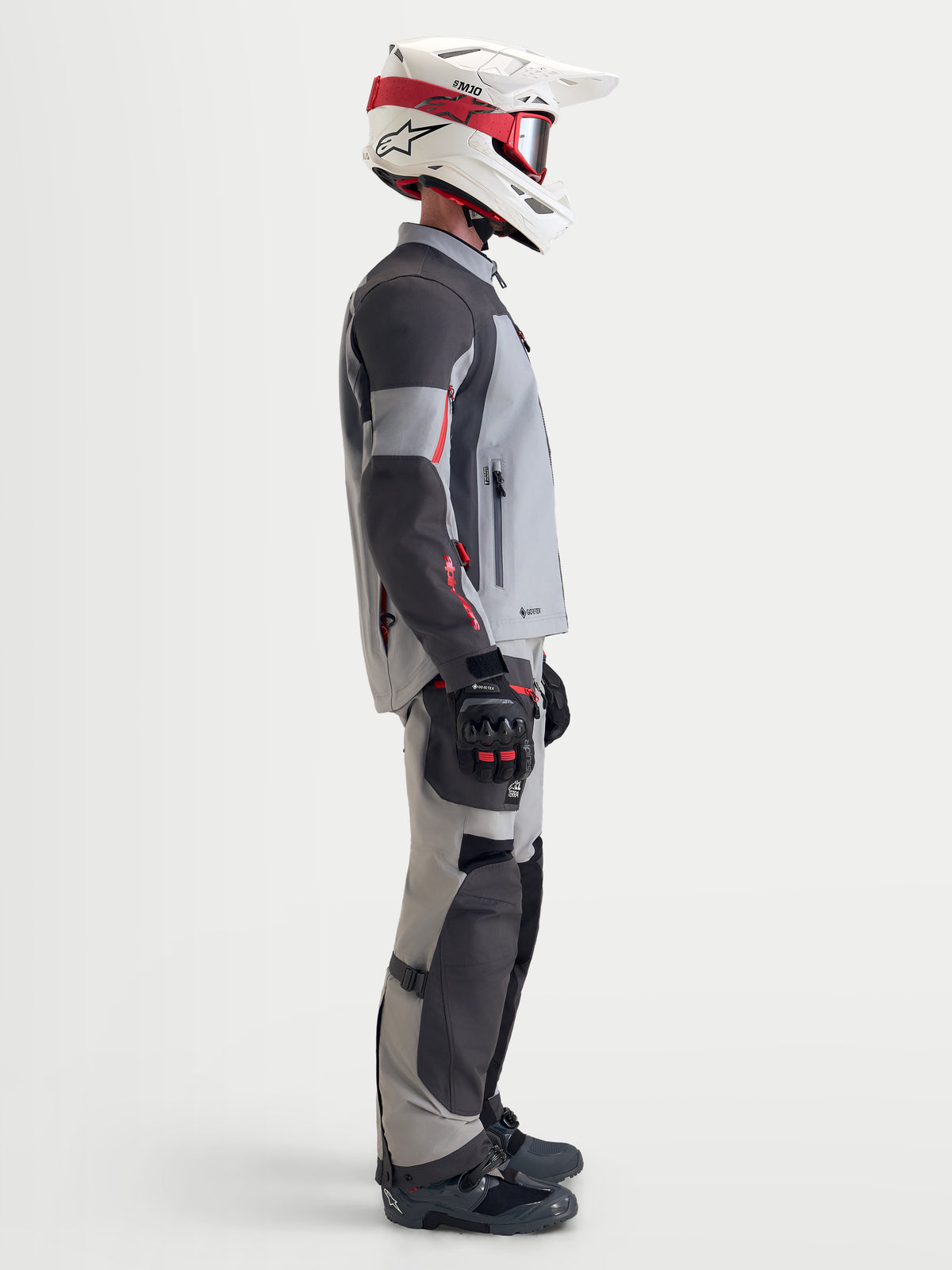 Alpinestars Arenis Gore-Tex Jacke, Herren-Adventure-Motorradjacke in Mittelgrau, Dunkelgrau und Schwarz, Seitenprofil eines Fahrers mit der wasserdichten Textiljacke, passender Ausrüstung sowie einem weiß-roten Helm