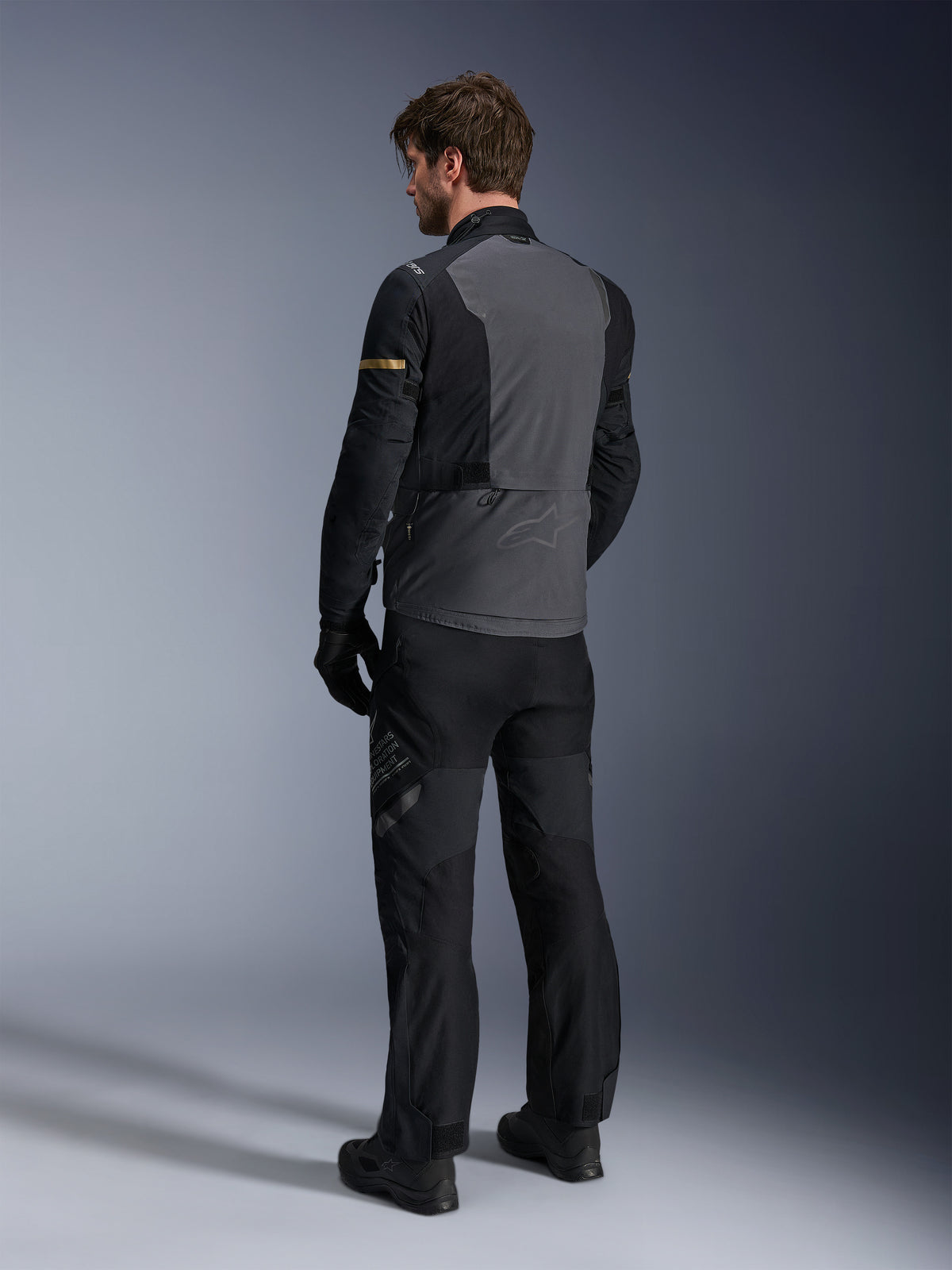 Alpinestars ST-7 2L GORE-TEX Jacke, Dunkelgrau und Schwarz mit Akzenten in Dark Khaki, Rückansicht eines Fahrers, der die Jacke und die passende Motorradhose trägt, Adventure-Touring-Ausrüstung mit wasserdichter laminierter Konstruktion