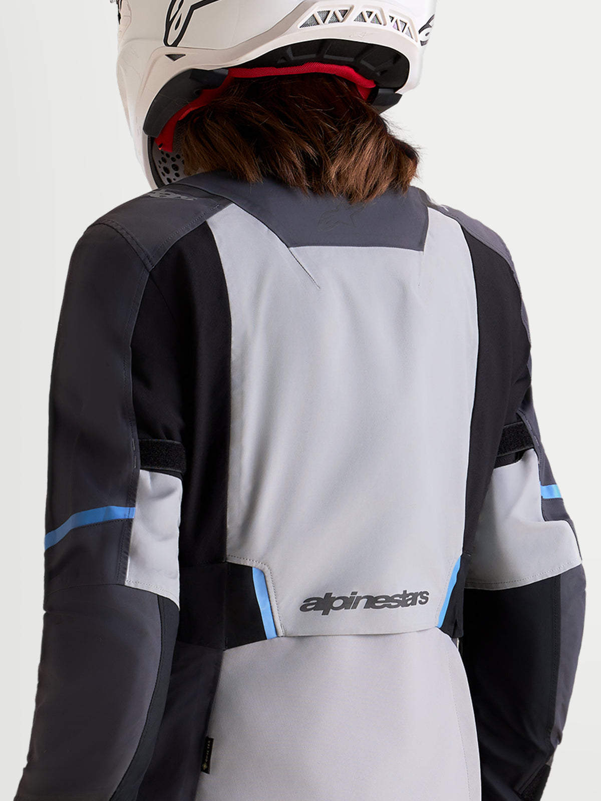 Alpinestars Stella ST-7 V2 2L Gore-Tex Jacket, women's adventure touring motorcycle jacket in mid gray, deep gray, and black, rear profile view on a model wearing matching gear and helmet, showing waterproof textile construction and branding details.