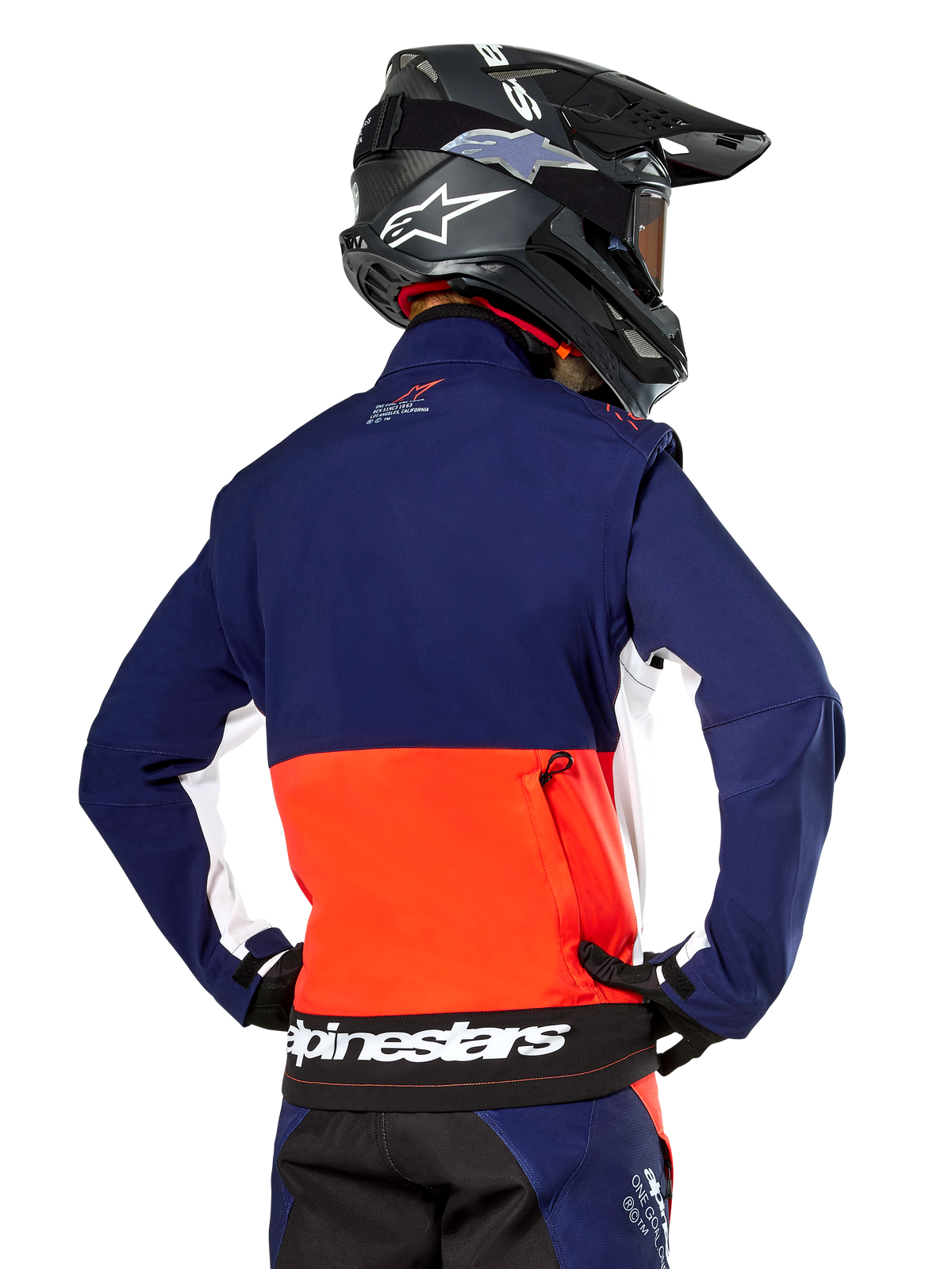 Alpinestars Lite-Dura Softshell-Jacke, Marineblau, Hot Orange und Weiß, Rückansicht getragen von einem Motocross-Fahrer, mit großem weißem Logo am Rückensaum und Reißverschlusstasche, Teil eines kompletten Offroad-Rennoutfits.