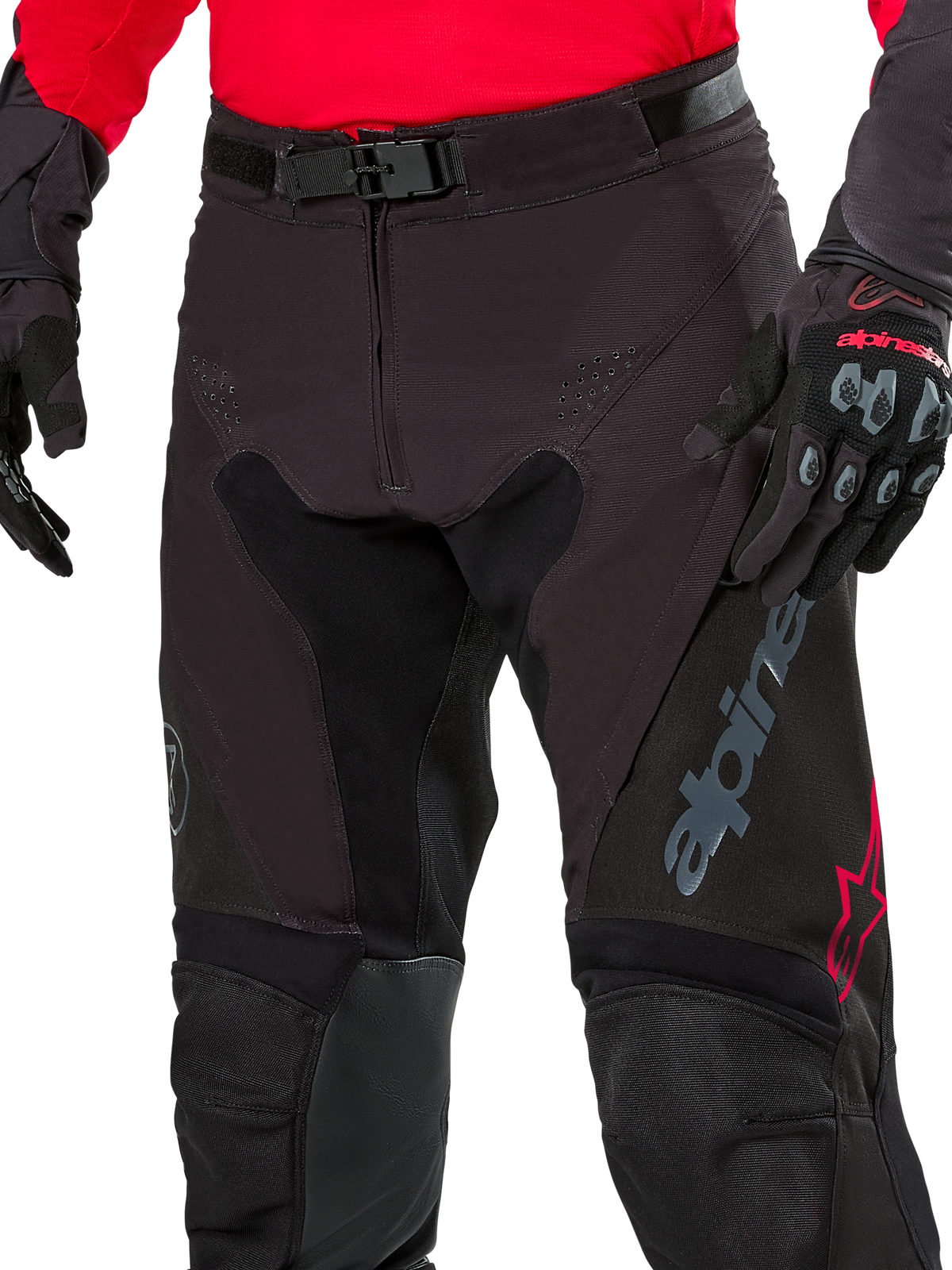 Nahaufnahme der Alpinestars Pro-Dura Hose, Enduro-Hose, Black Magnet White mit roten Akzenten, mit sicherem Magnet-Schnallenverschluss und Reißverschluss, getragen mit passendem rotem Trikot und schwarzen Handschuhen, strapazierfähige Ripstop-Konstruktion für das Offroad-Fahren