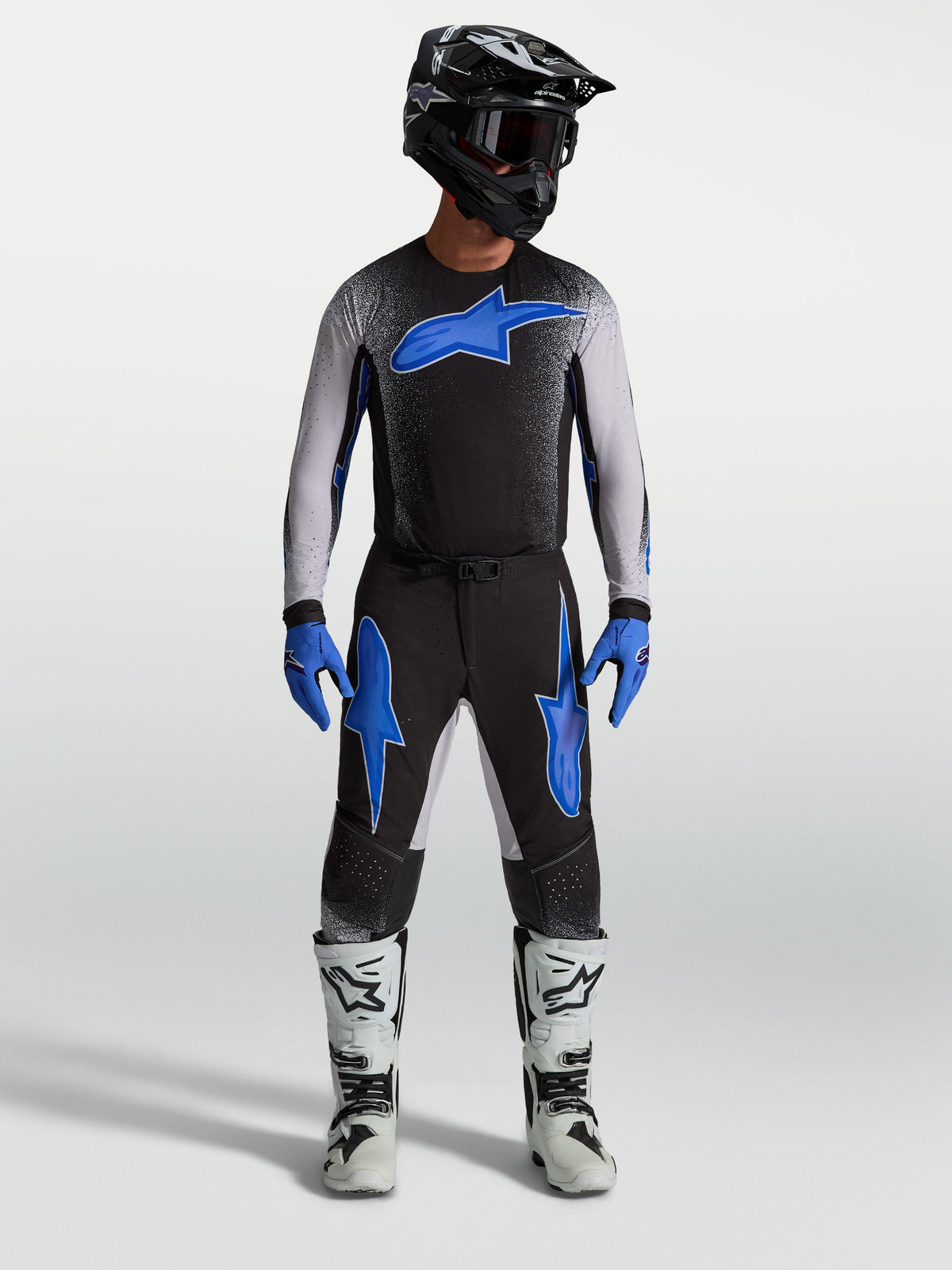 Alpinestars Supertech Hiten AFD Hose, Motocross-Hose für Herren, Schwarz und Blau, am Model mit passendem Trikot und weißen Motorradstiefeln, professionelle Offroad-Rennsport-Ausrüstung