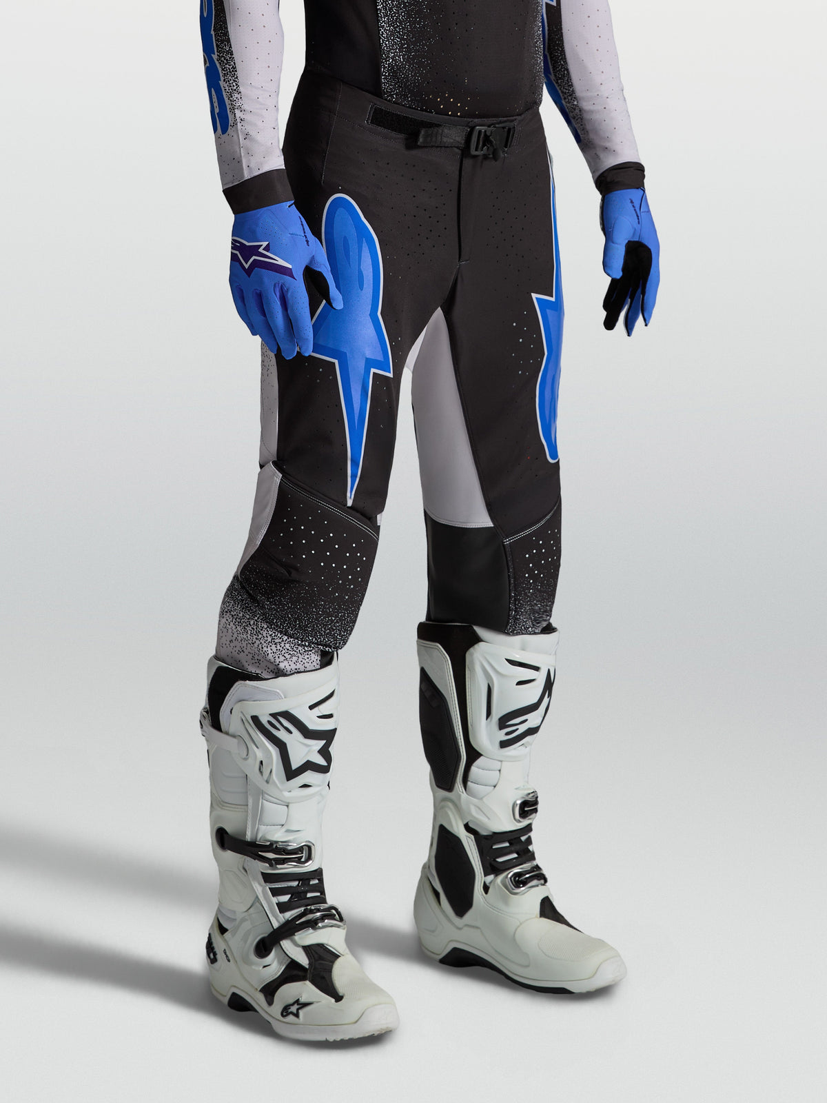 Alpinestars Supertech Hiten AFD Hose, Herren-Motocrosshose in Schwarz und Blau, athletische Passform für professionellen Rennsport, getragen mit weißen Offroad-Stiefeln.
