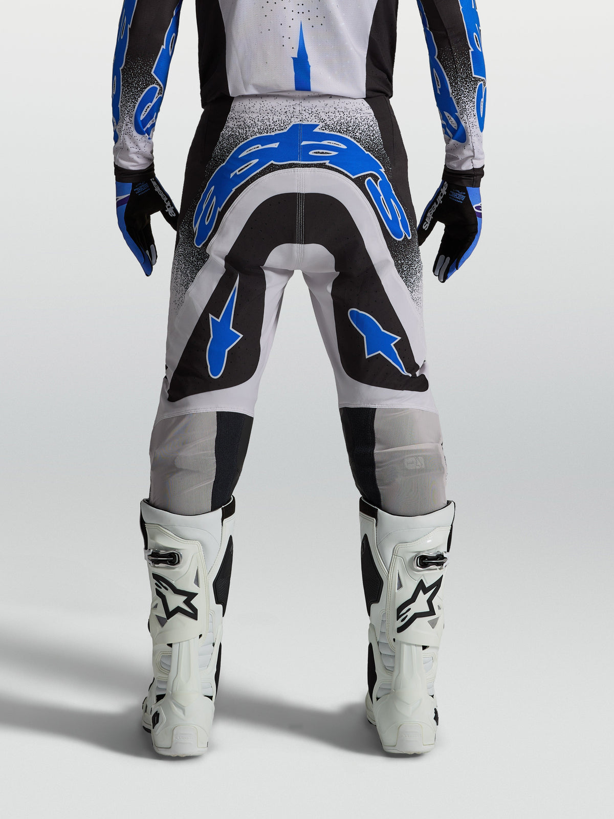 Alpinestars Supertech Hiten AFD Hose, Herren-Motocross-Hose in Schwarz und Blau, athletische Rennpassform, Rückansicht am Model mit weißen Stiefeln.