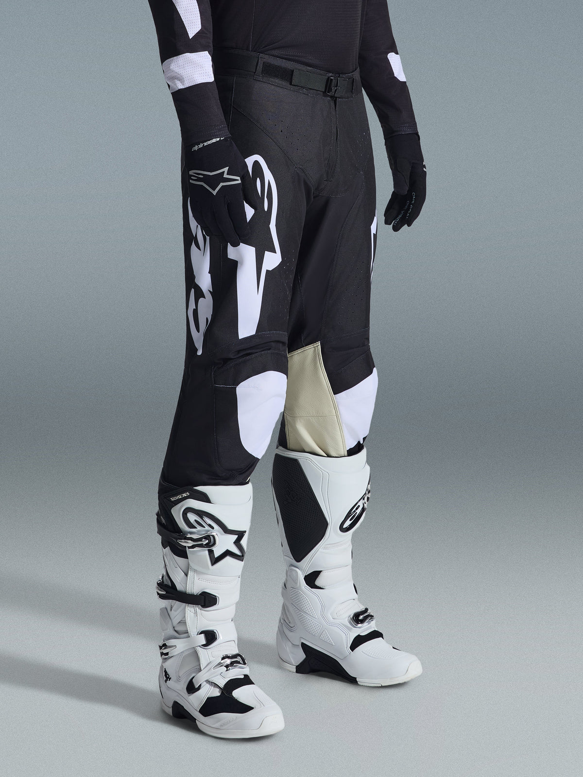 Alpinestars 2026 Racer Air Riway Hose, Motocross-Hose, Schwarz und Weiß, getragen mit weiß-schwarzen Tech Series Stiefeln und schwarzem Langarmtrikot, mit weißem Alpinestars-Branding, lasergeschnittenen Perforationen und hellbraunen Knie-Einsätzen aus Ziegenleder für Offroad-Performance.