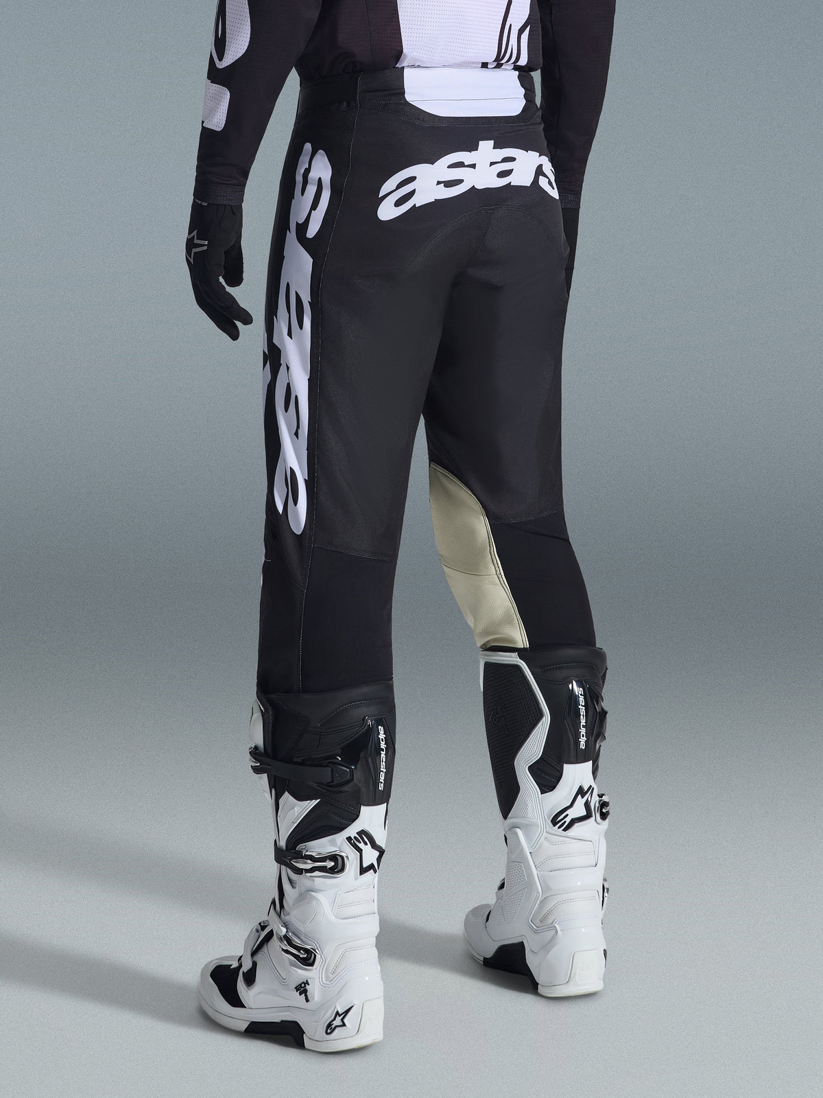 Alpinestars 2026 Racer Air Riway Hose, Motocross-Hose, Schwarz und Weiß, Rückansicht mit großem weißem Astars-Branding auf dem Gesäß und den Beinen, beigefarbene Leder-Einsätze an den Knieinnenseiten, getragen mit weiß-schwarzen Tech 7 Stiefeln, hochwertige Offroad-Rennbekleidung.