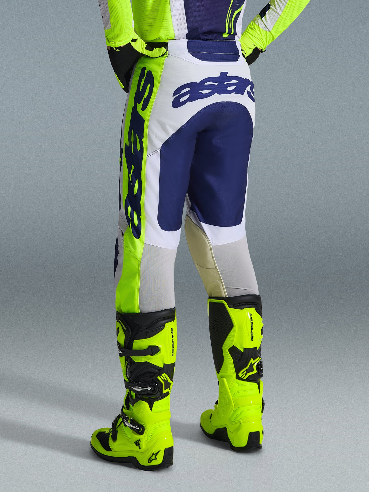 Alpinestars 2026 Racer Air Riway Hose, Motocross-Hose, Hellgrau, Gelb Fluo und Blau, Rückansicht mit markantem blauem Branding auf der Sitzfläche, getragen mit passendem Trikot und leuchtend gelben Fluo-Stiefeln, ergonomisches Race-Fit-Design