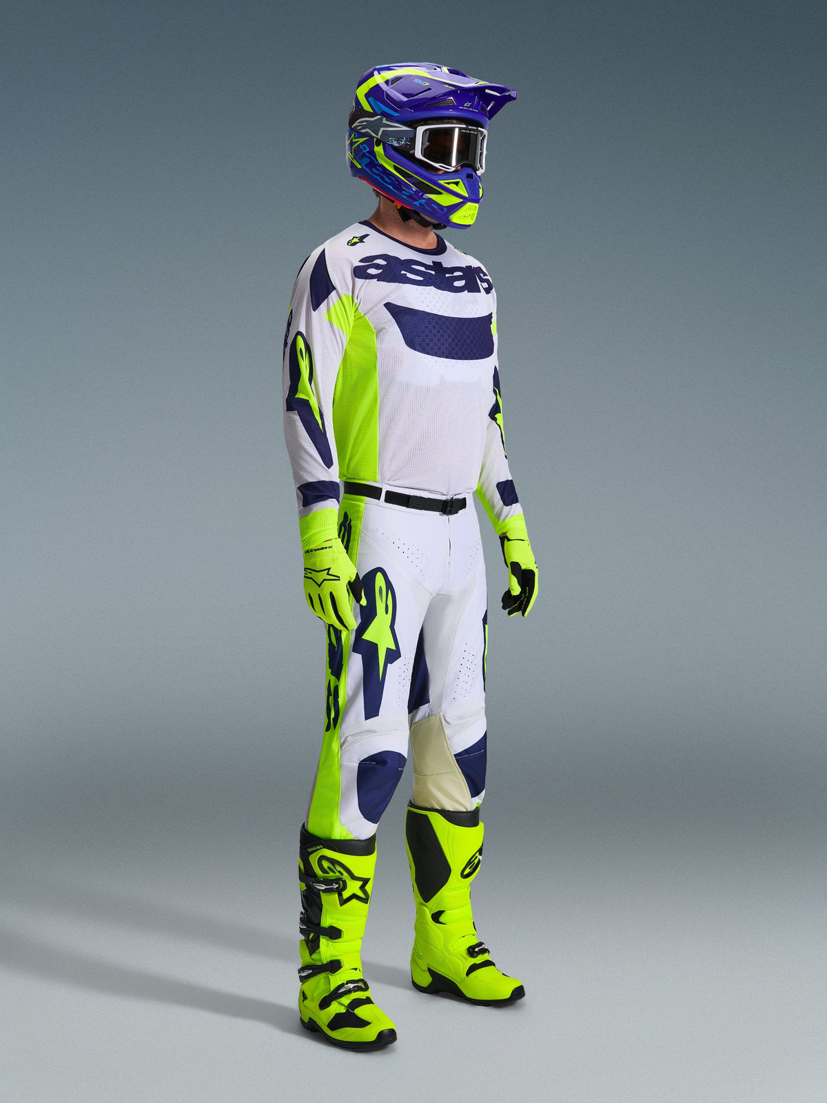Motocross-Fahrer in kompletter Rennausrüstung, 2026 Racer Air Riway Hose in Hellgrau Gelb Fluo Blau, passendes weiß-blaues Trikot, fluorgelbe Handschuhe und Stiefel sowie ein blau-gelber Helm, koordiniertes Outfit für professionelle Offroad-Performance
