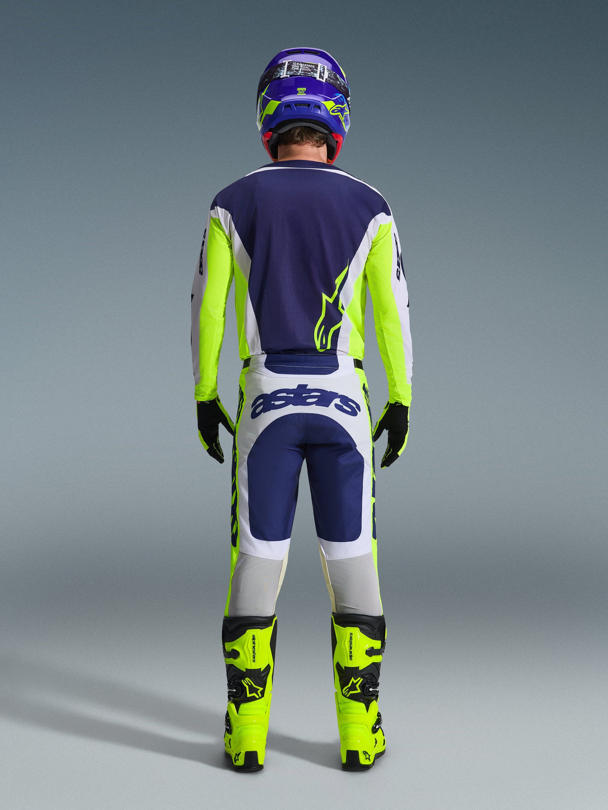 Motocross-Fahrer in der Rückansicht mit der Alpinestars 2026 Racer Air Riway Hose in Hellgrau, Gelb Fluo und Blau, kombiniert mit einem passenden Trikot und leuchtend gelben Stiefeln, zur Darstellung einer kompletten professionellen Offroad-Rennausrüstung.