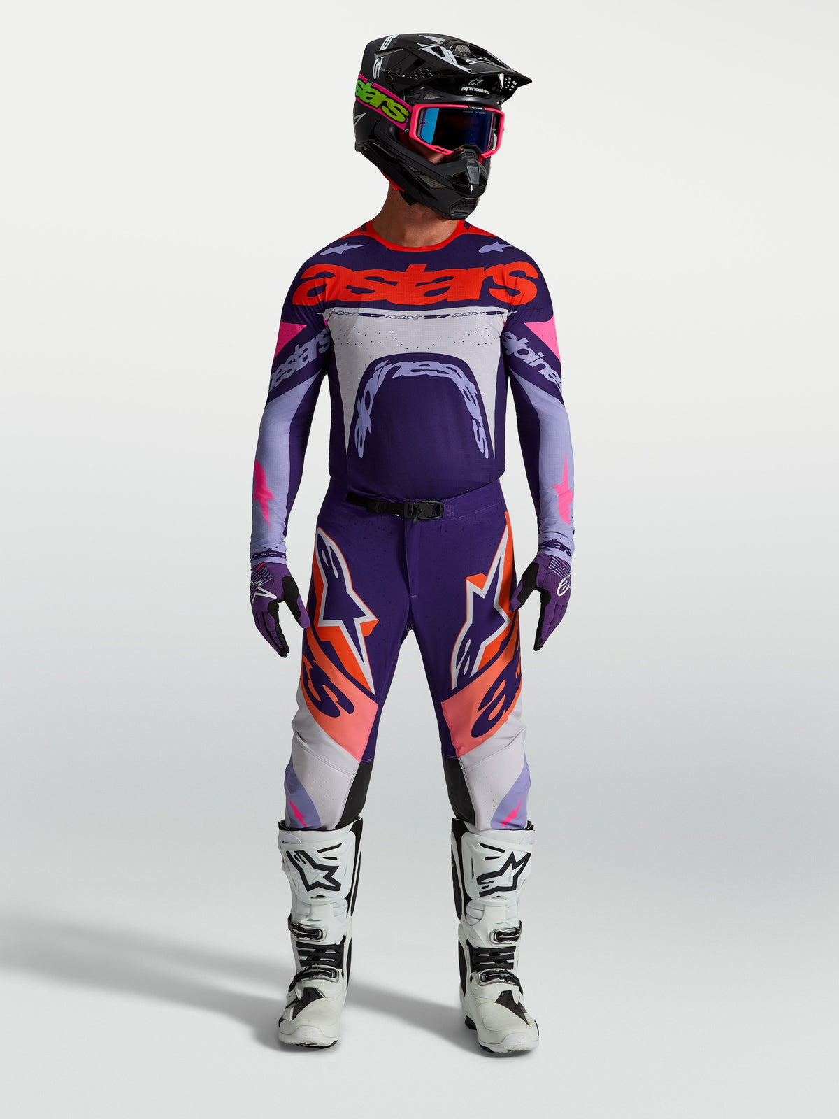 Alpinestars Supertech Dyna Hose und Trikot, Herren Motocross-Set in Lila und Pink Fluo, am Model mit Helm und Stiefeln.