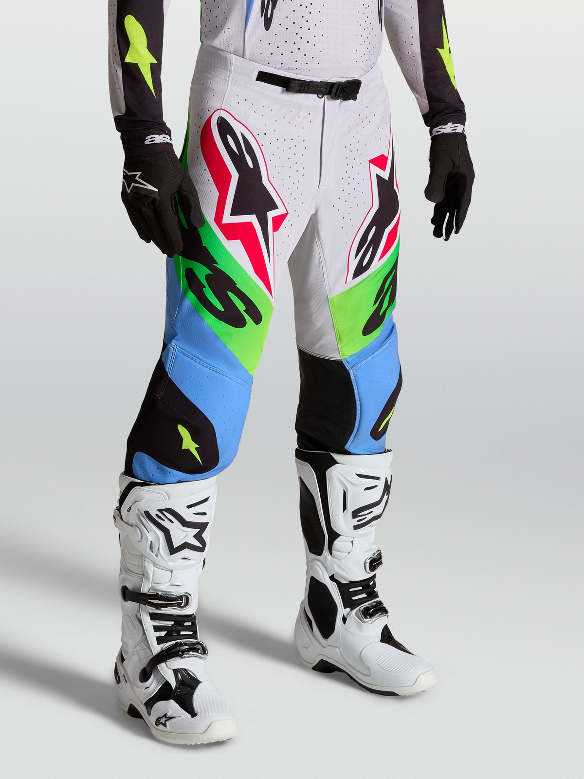 Alpinestars Supertech Dyna Hose, Motocross-Hose in Blau und Grün, Modell trägt weiße Motorradstiefel und schwarze Handschuhe, professionelle MX-Rennhose