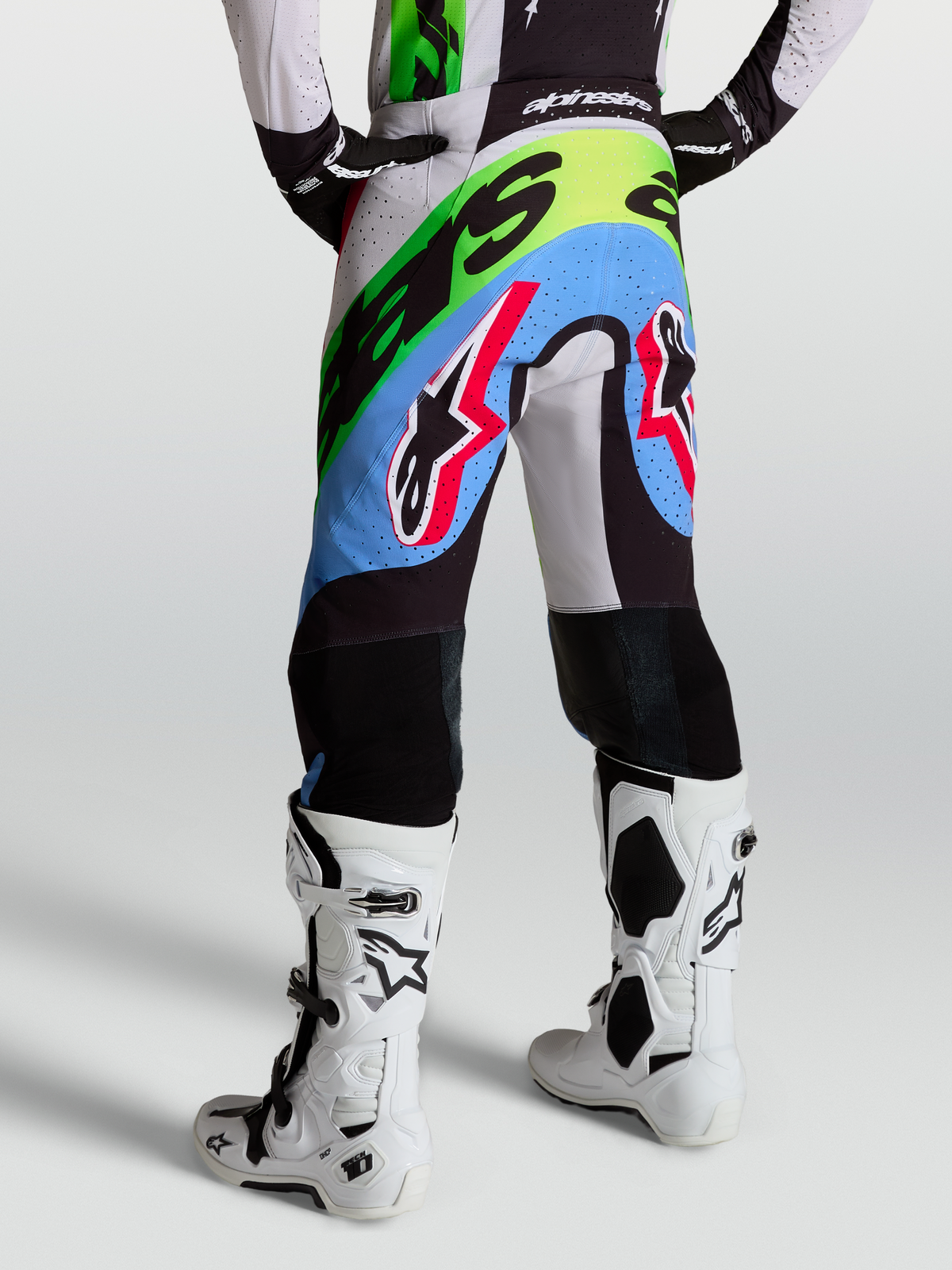 Alpinestars Supertech Dyna Hose, Motocross-Rennsport-Hose für Herren, Flieder, Grün und Schwarz, Rückansicht mit perforiertem Stretch-Ripstop-Gewebe und Ziegenleder-Kniepanels, getragen mit weißen Tech 10 Stiefeln.
