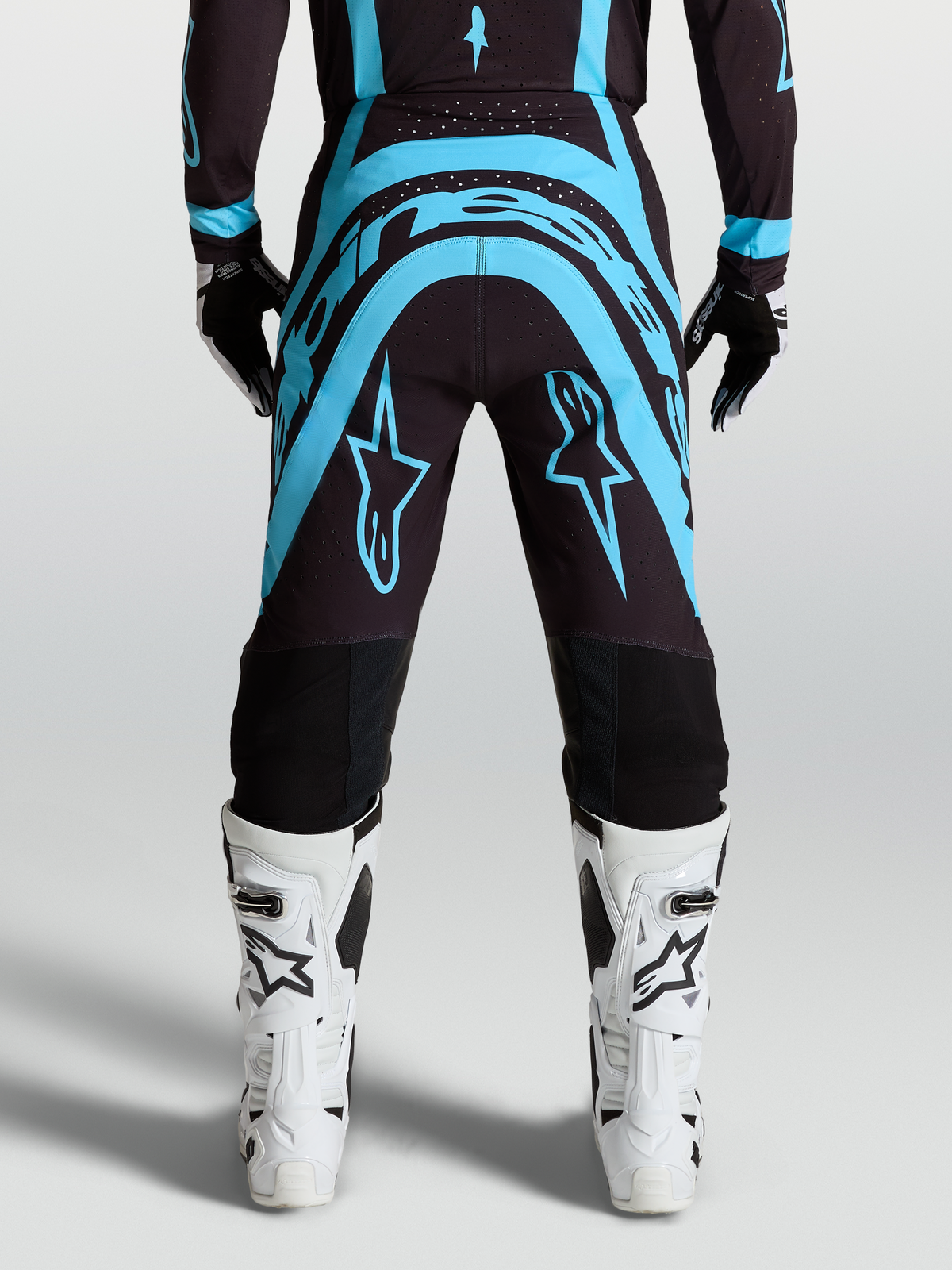 Alpinestars Supertech Vesta Motocross Pants, Black and Turquoise race-fit pants with White off-road riding boots.