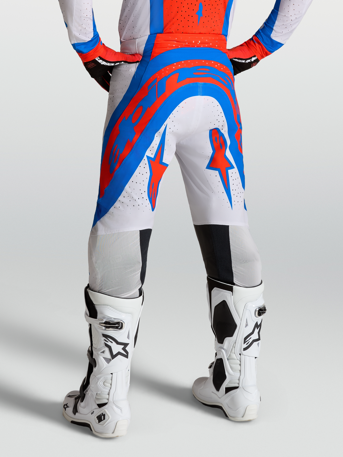 Alpinestars Supertech Vesta Hose, Motocross-Performance-Hose in Blau, Rot und Weiß, athletische Rennpassform mit Stretchnet-Zonen und Ripstop-Gewebe, getragen mit weißen Tech 10 Stiefeln.