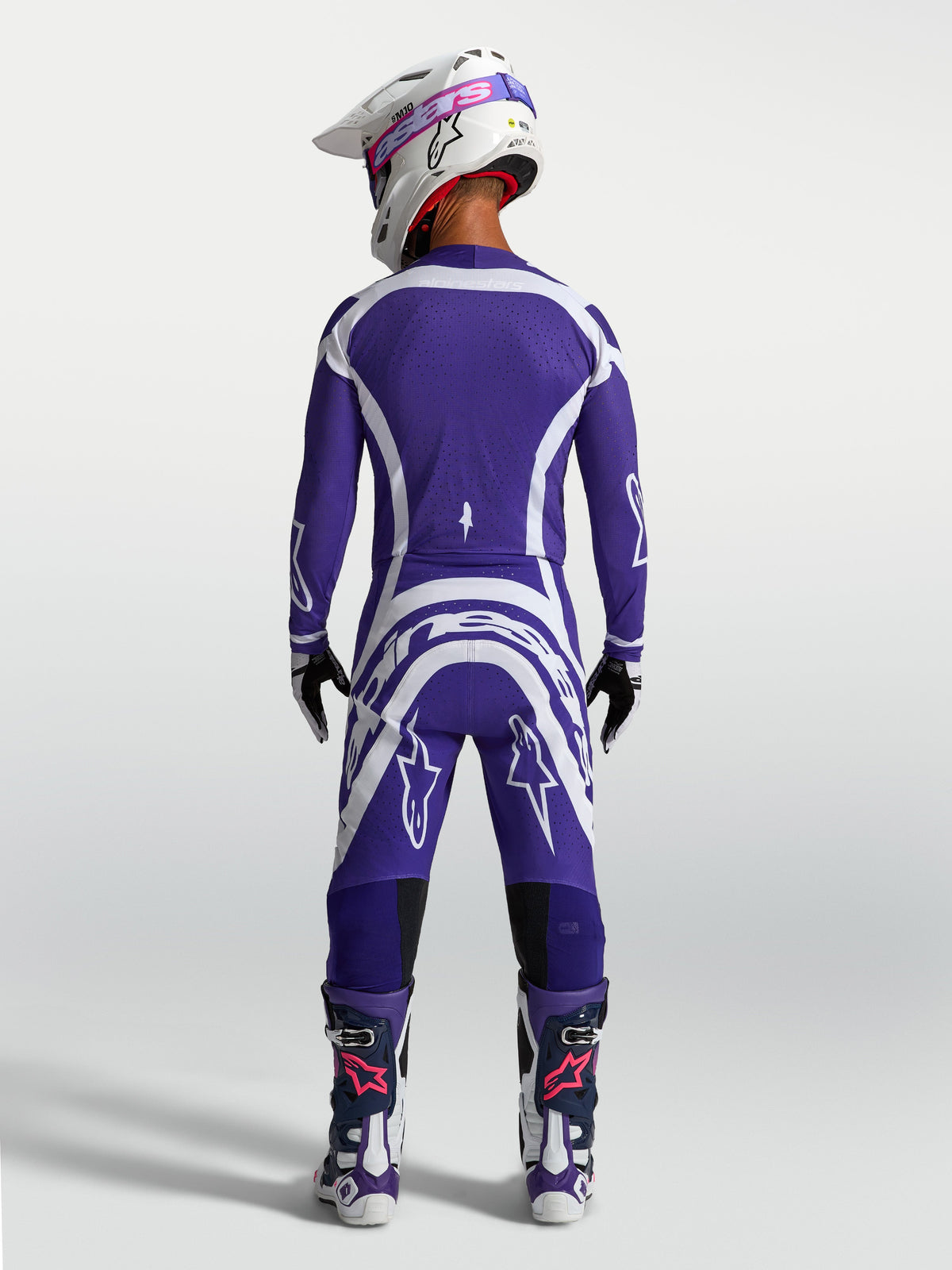 Alpinestars Supertech Vesta Trikot und Hose, Motocross-Rennausrüstung in Blau und Weiß, Rückansicht am Model mit Helm und Stiefeln.