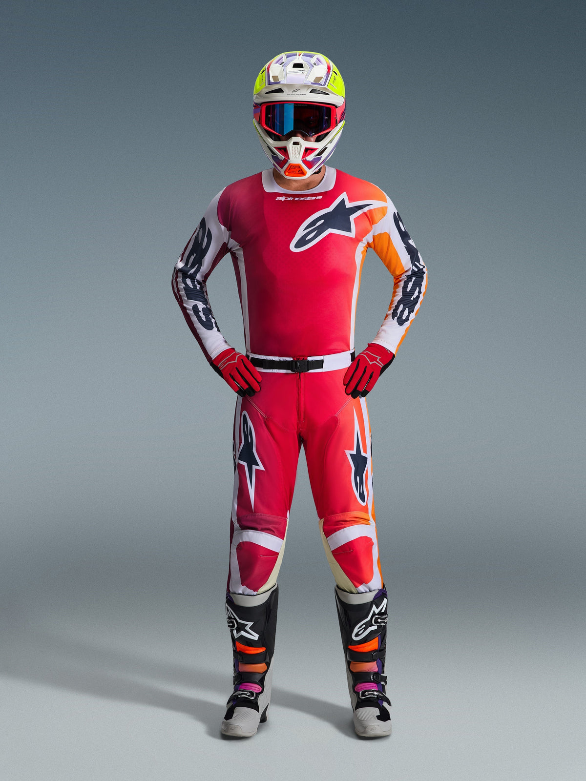 Motocross rider wearing complete racing gear, Red jersey with white and orange accents, 2026 Racer Portl Pants in red and white, white helmet with colorful accents and blue goggles, red gloves, and black and gray boots, coordinated outfit for off-road performance