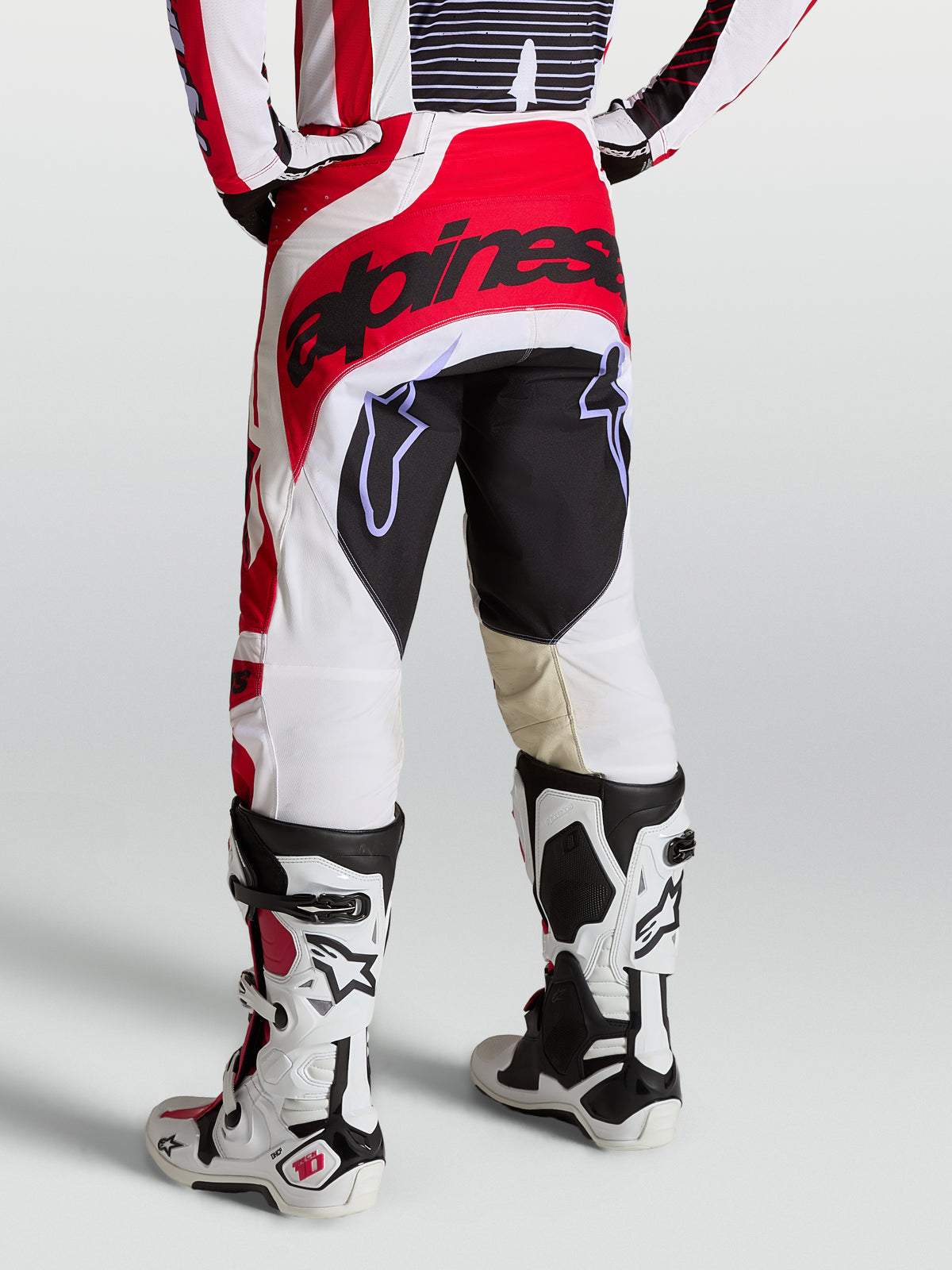 Alpinestars Techstar Maven Hose, Motocross-Hose für Herren, Rückansicht in Rot und Weiß, verstärkter Sitzbereich und athletische Rennpassform, getragen mit weißen Tech 10 Stiefeln.