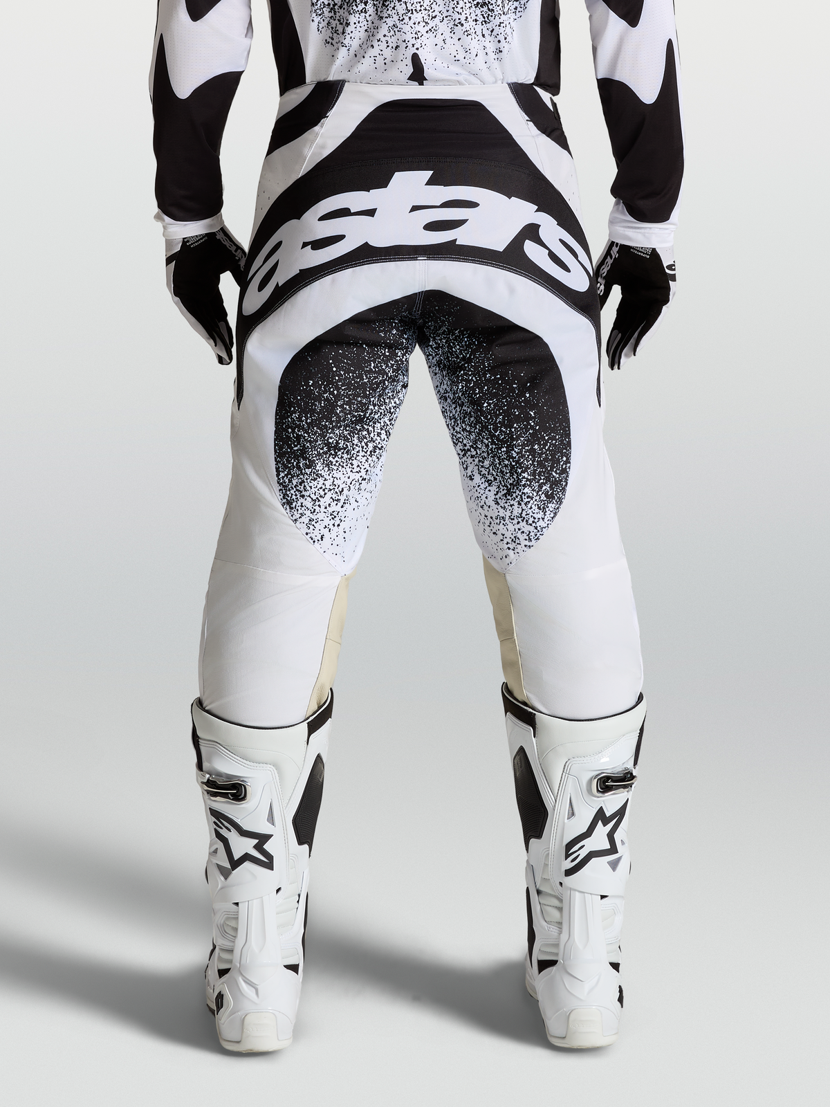 Alpinestars Techstar Swan Hose, Motocross-Hose in Schwarz und Weiß, Rückansicht mit großem Astar-Logo am Gesäß, Babel-Kniekonstruktion, getragen mit weißen Motorradstiefeln für den Offroad-Einsatz.