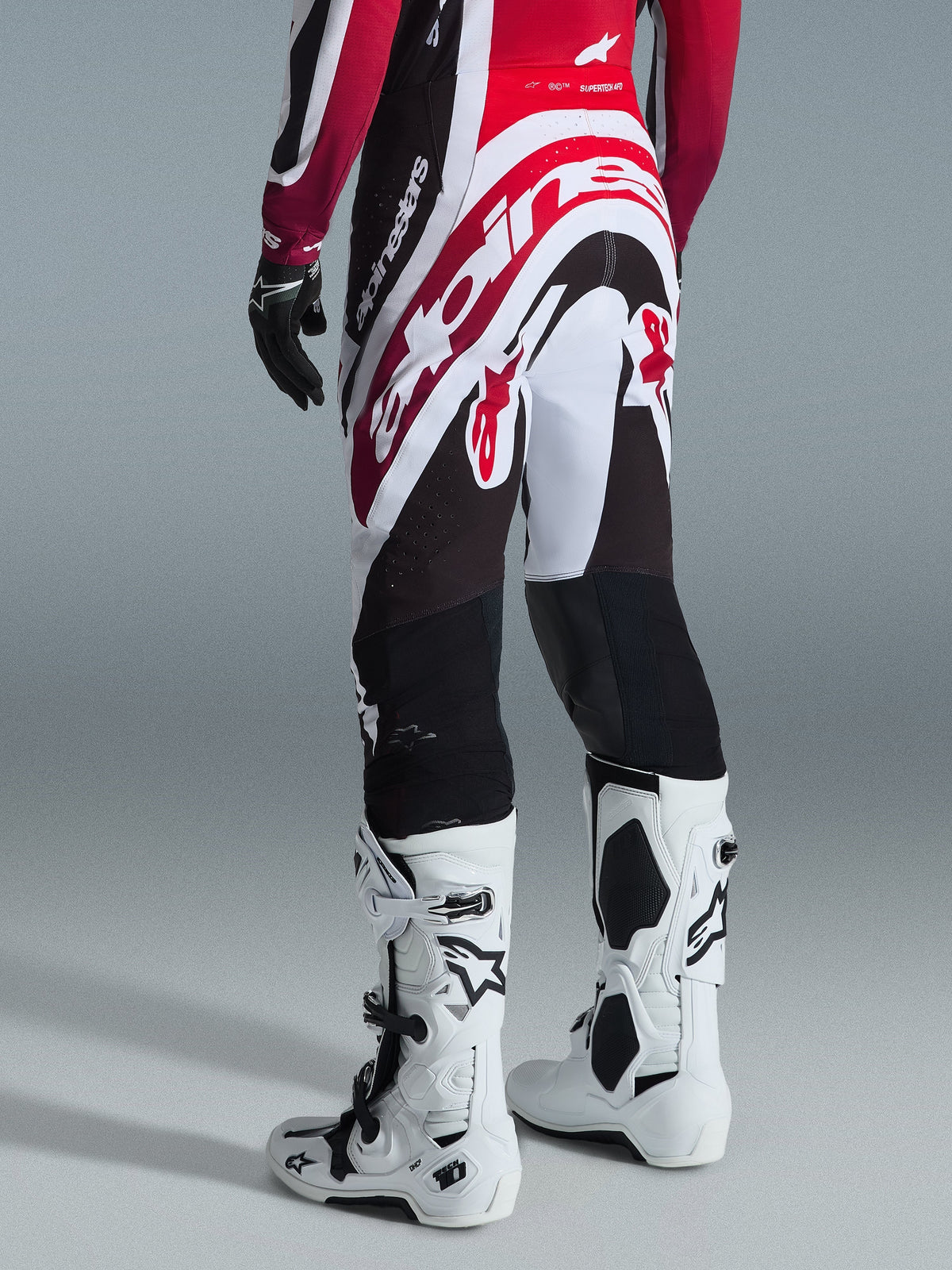 Alpinestars 2026 Supertech AFD Vista Pants, Motocross Pants, Black Red and White, rear view on a rider, worn with white Tech 10 boots and a matching jersey, athletic race-fit design for elite off-road performance