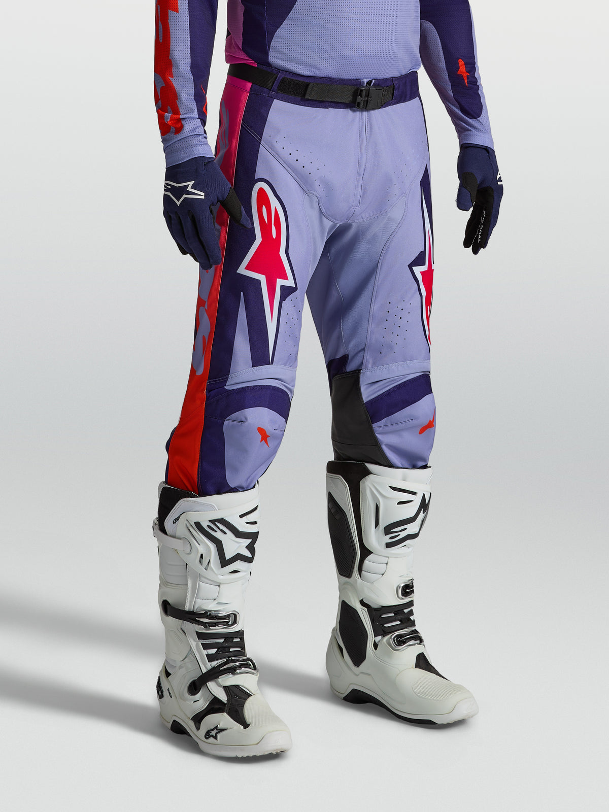 Alpinestars Racer Air Hunt Hose, belüftete Motocross-Ausrüstung in Lila und Pink, am Modell mit weißen Stiefeln.