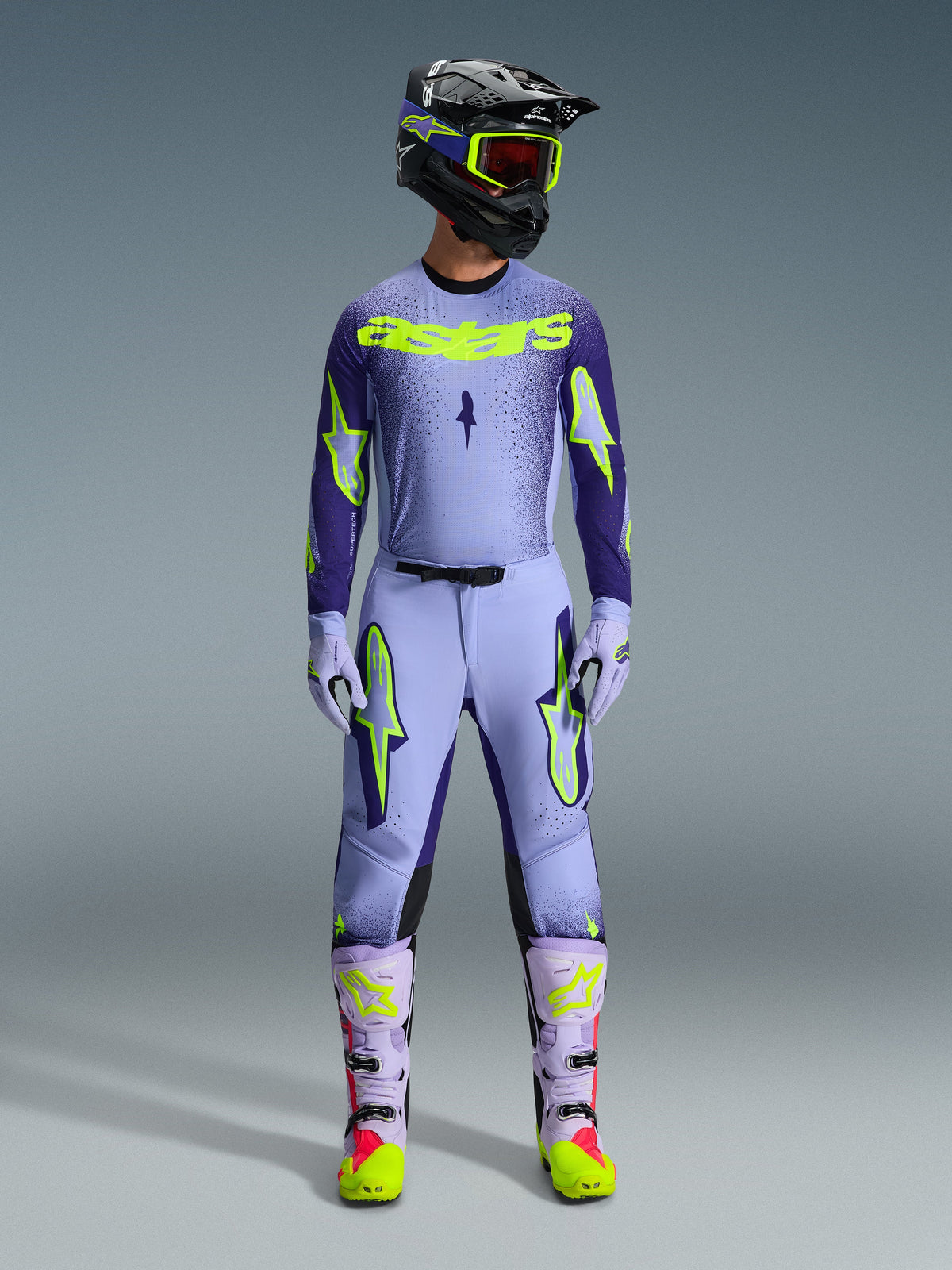 Alpinestars 2026 Supertech Scenz Hose, Motocross-Hose, Purple Yellow Fluo, getragen als komplettes Rennbekleidungsset mit passendem lavendelfarbenem Trikot, Handschuhen und Stiefeln, mit markanten neongelben Logos, athletische Passform für professionellen Offroad-Rennsport.