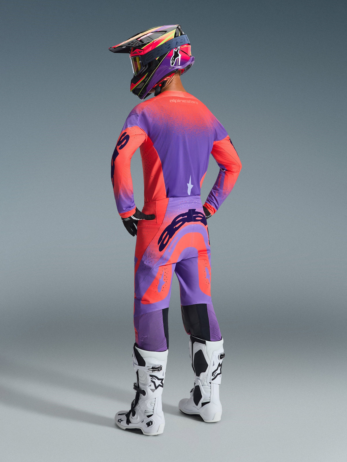 Alpinestars 2026 Supertech Scenz Hose, Motocross-Hose, Hot Coral und Lila, Rückansicht mit markantem Branding am Gesäß, getragen von einem Fahrer mit passendem Jersey und weißen Stiefeln, professionelle Offroad-Rennausrüstung.