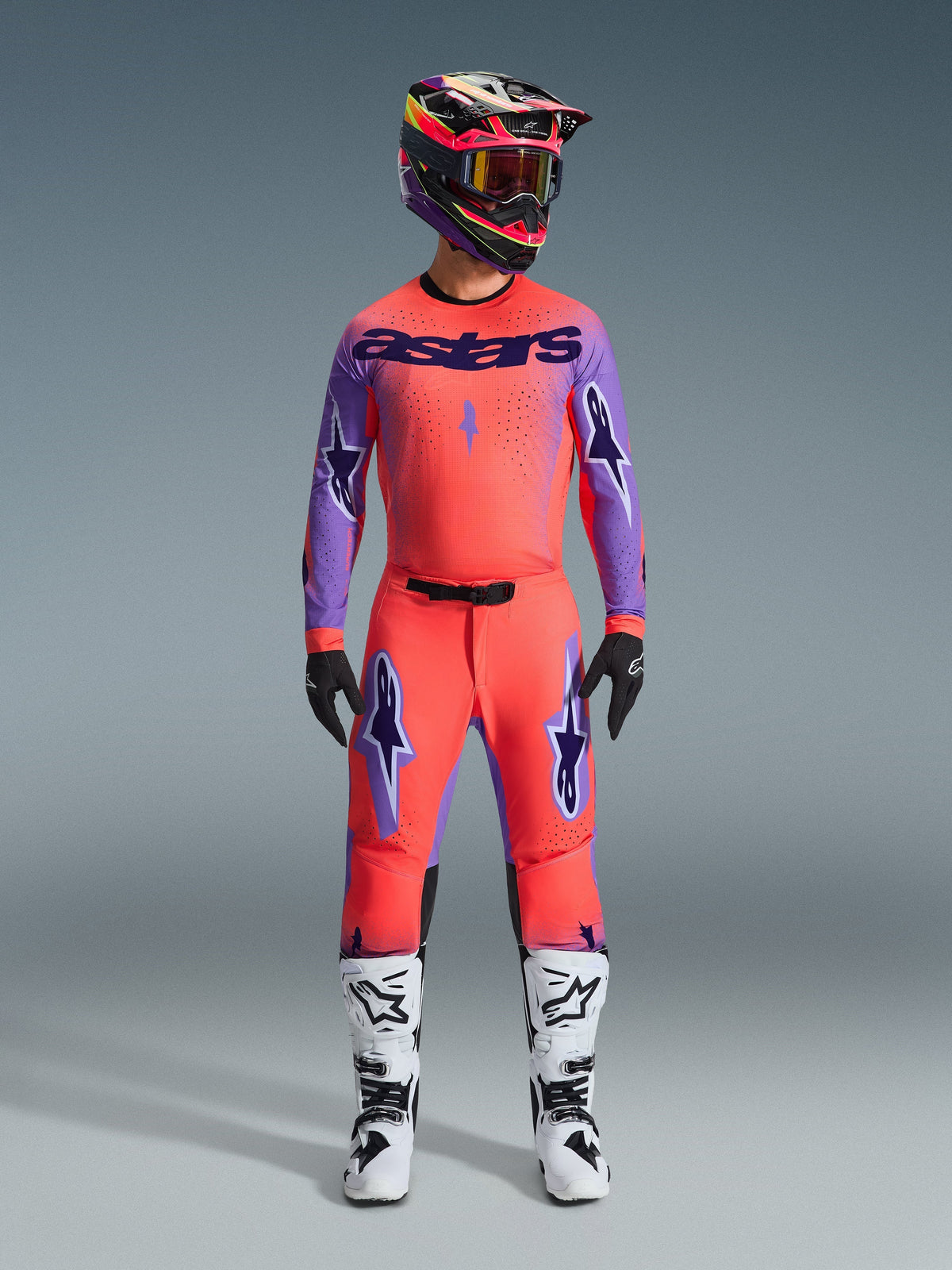 Alpinestars 2026 Supertech Scenz Hose, Motocross-Hose, Hot Coral und Lila, getragen als komplettes Gear-Set mit passendem Trikot und Helm, weiße und schwarze Stiefel, mit lila Logos und athletischer Race-Passform.