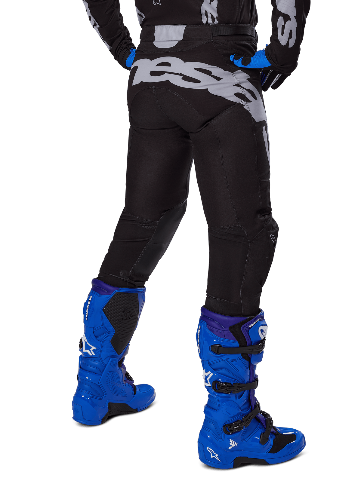 Alpinestars 2025 Racer Graphite Hose, Motocross-Hose, Schwarz und Grau, Rückansicht mit großem grauen Branding am Gesäß, getragen mit leuchtend blauen Motocross-Stiefeln und schwarz-blauem Trikot, strapazierfähige Offroad-Rennausrüstung